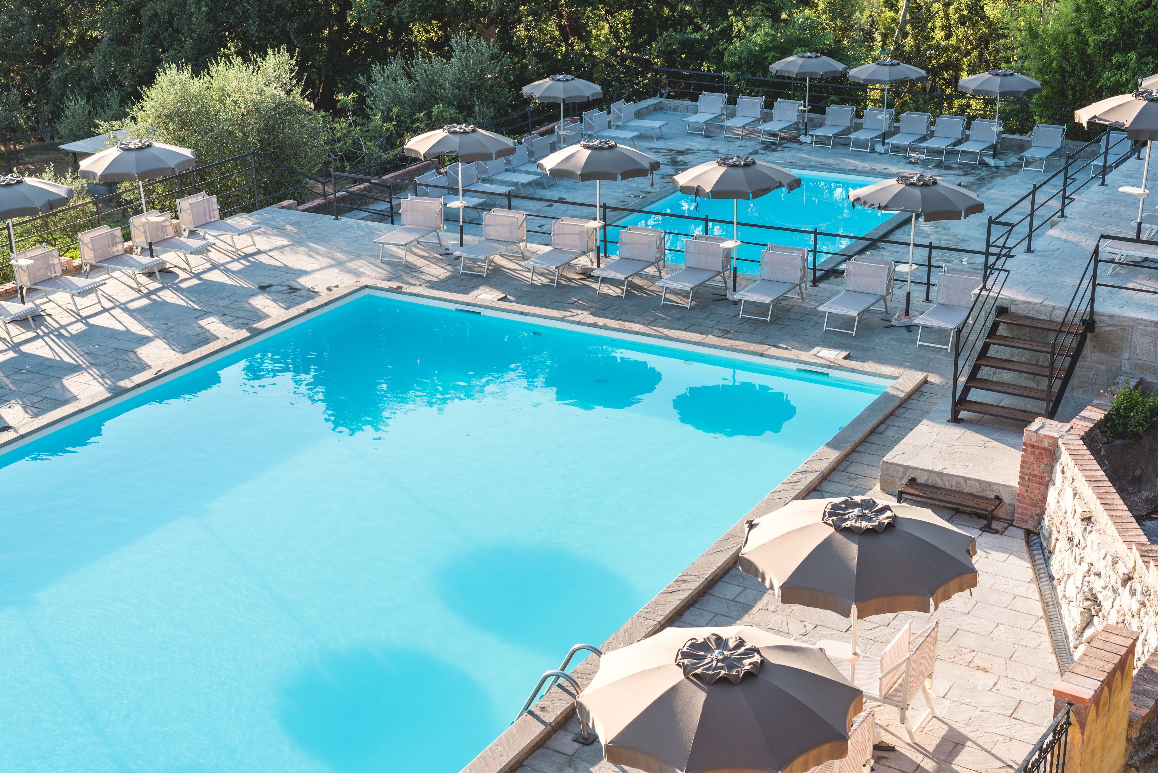 Une piscine entourée de murs de pierre et de verdure, avec des chaises longues et des parasols.