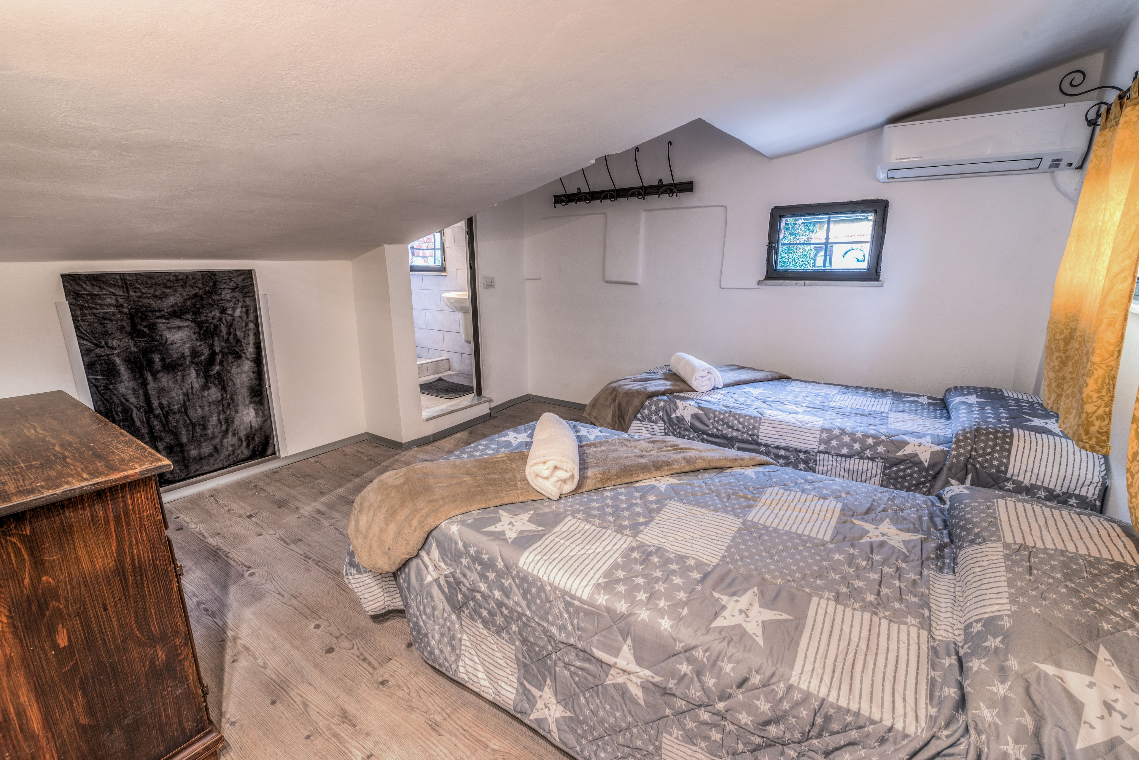 A bedroom with two beds, a wooden dresser, a window, and an air conditioning unit.