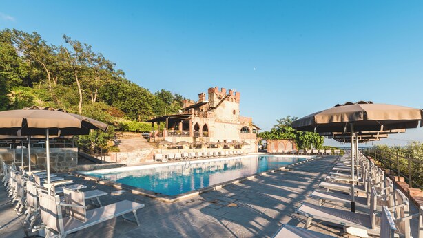 A pool area with lounge chairs and umbrellas, a castle-like building in the background, and a clear sky. - Ippotur Medieval Resort (Castelnuovo Magra)