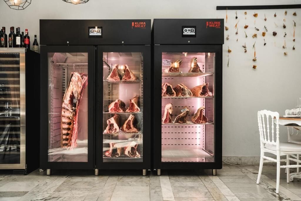 Trois unités de réfrigération noires, portant l’inscription « Klima Meat », et contenant différents morceaux de viande.
