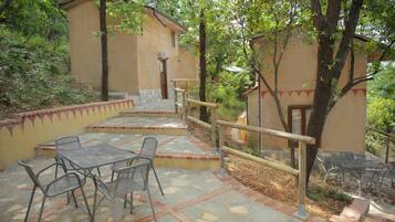Un patio con mesa y sillas, baranda de madera y un edificio con puerta y ventanas.