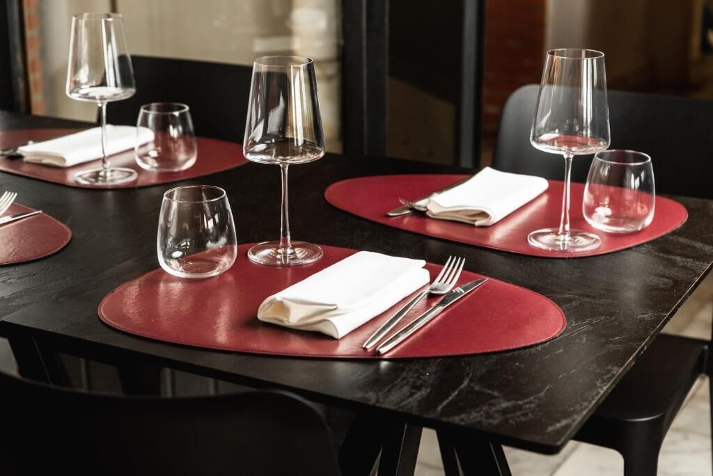 A restaurant table set with red placemats, wine glasses, and cutlery.