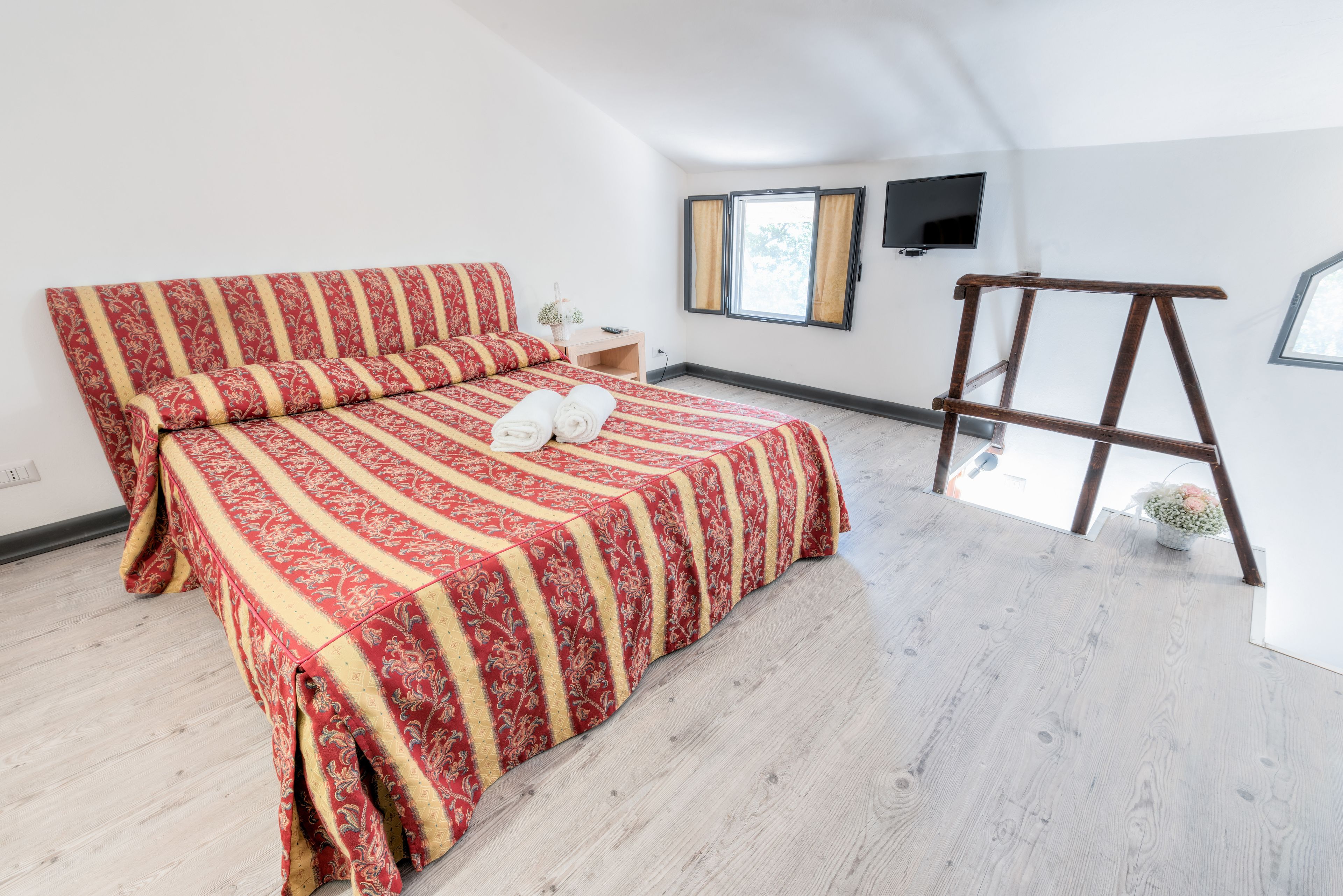 Un dormitorio con una cama grande, una escalera de madera, un televisor montado en la pared y una ventana con cortinas.