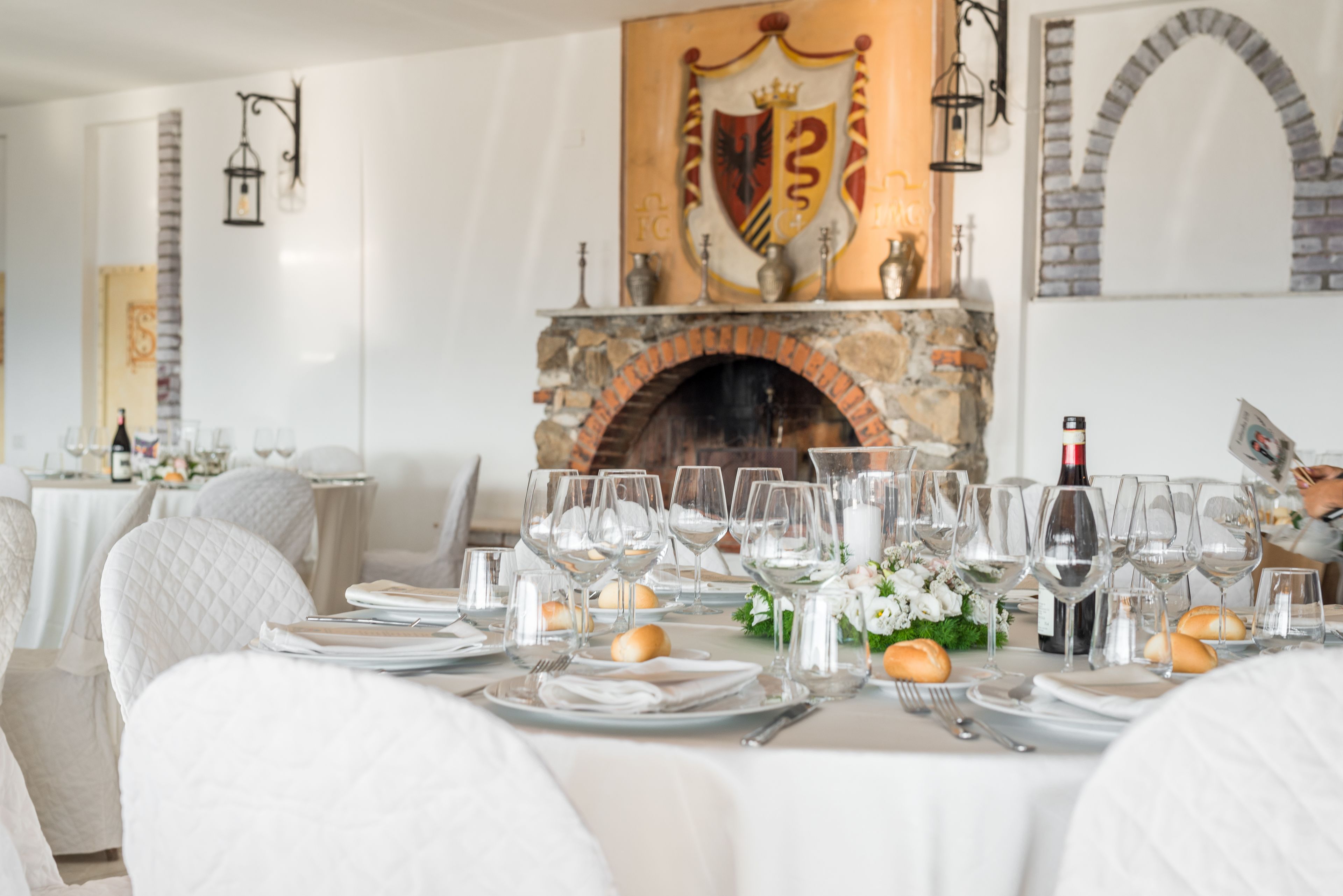 A formal dining room with a stone fireplace, white tablecloths, and neatly set tables.