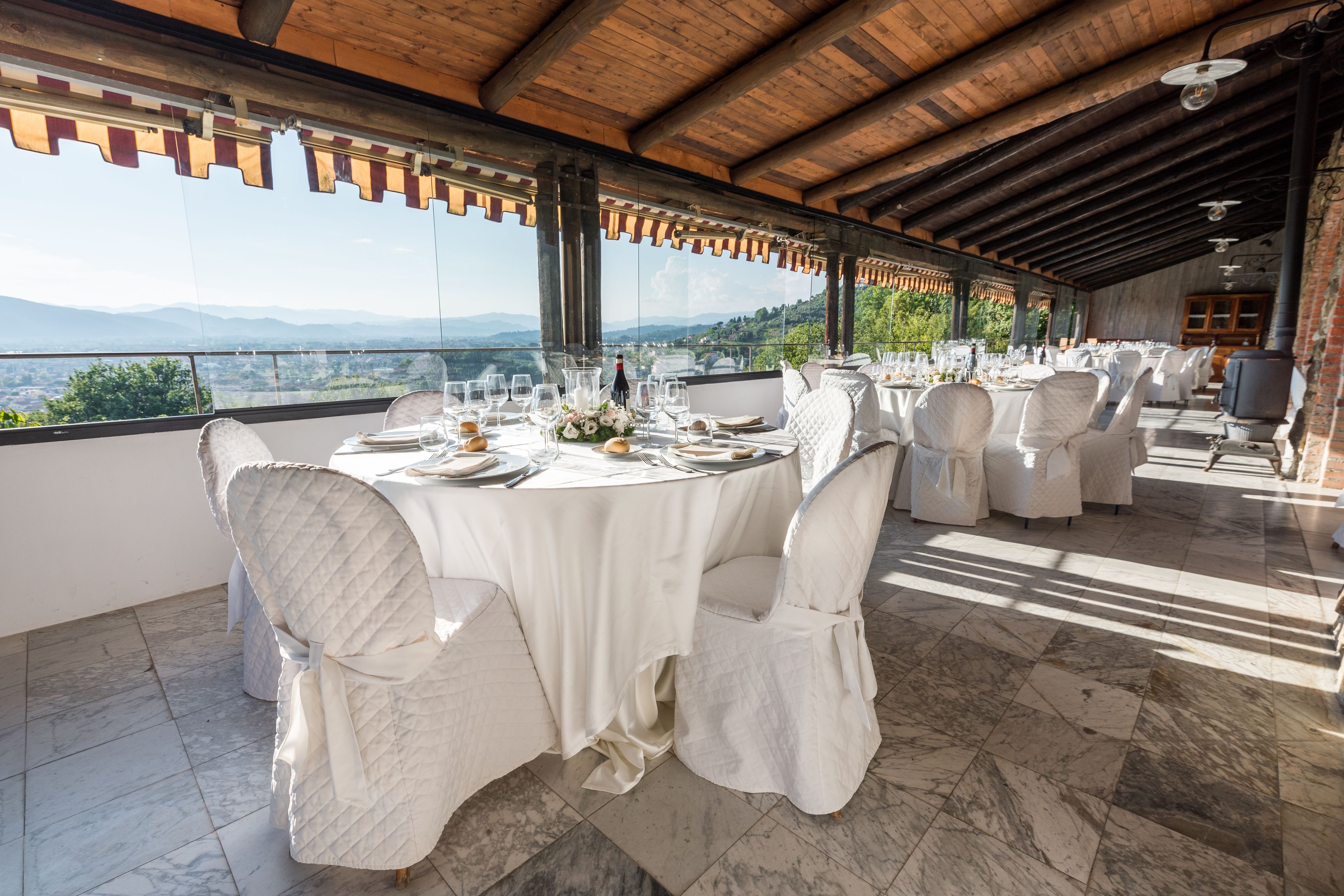 A restaurant with round tables set for dining, large windows offering a mountain view, and a wooden ceiling.