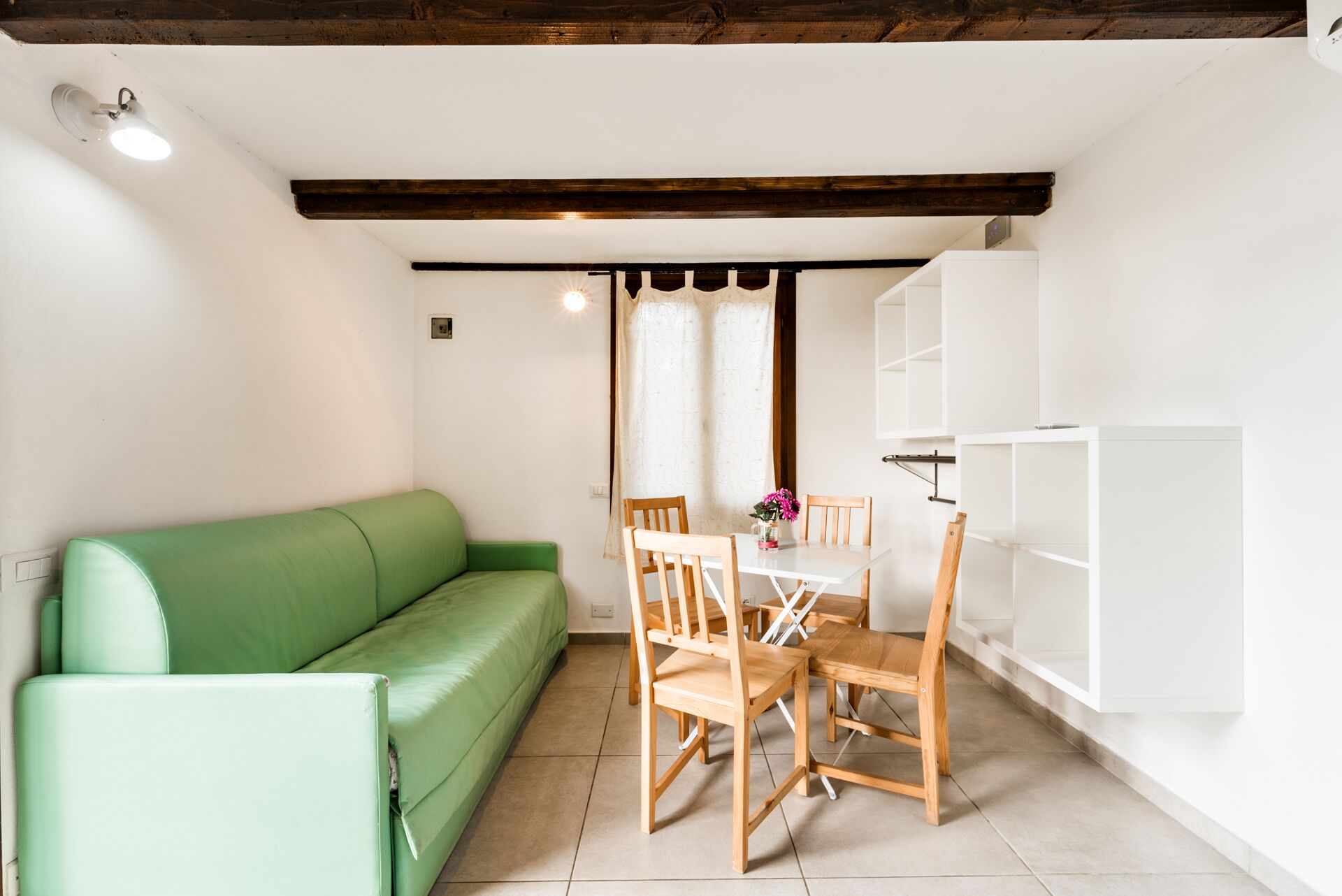 A room with a green sofa, wooden chairs, a white table, and a white cabinet.