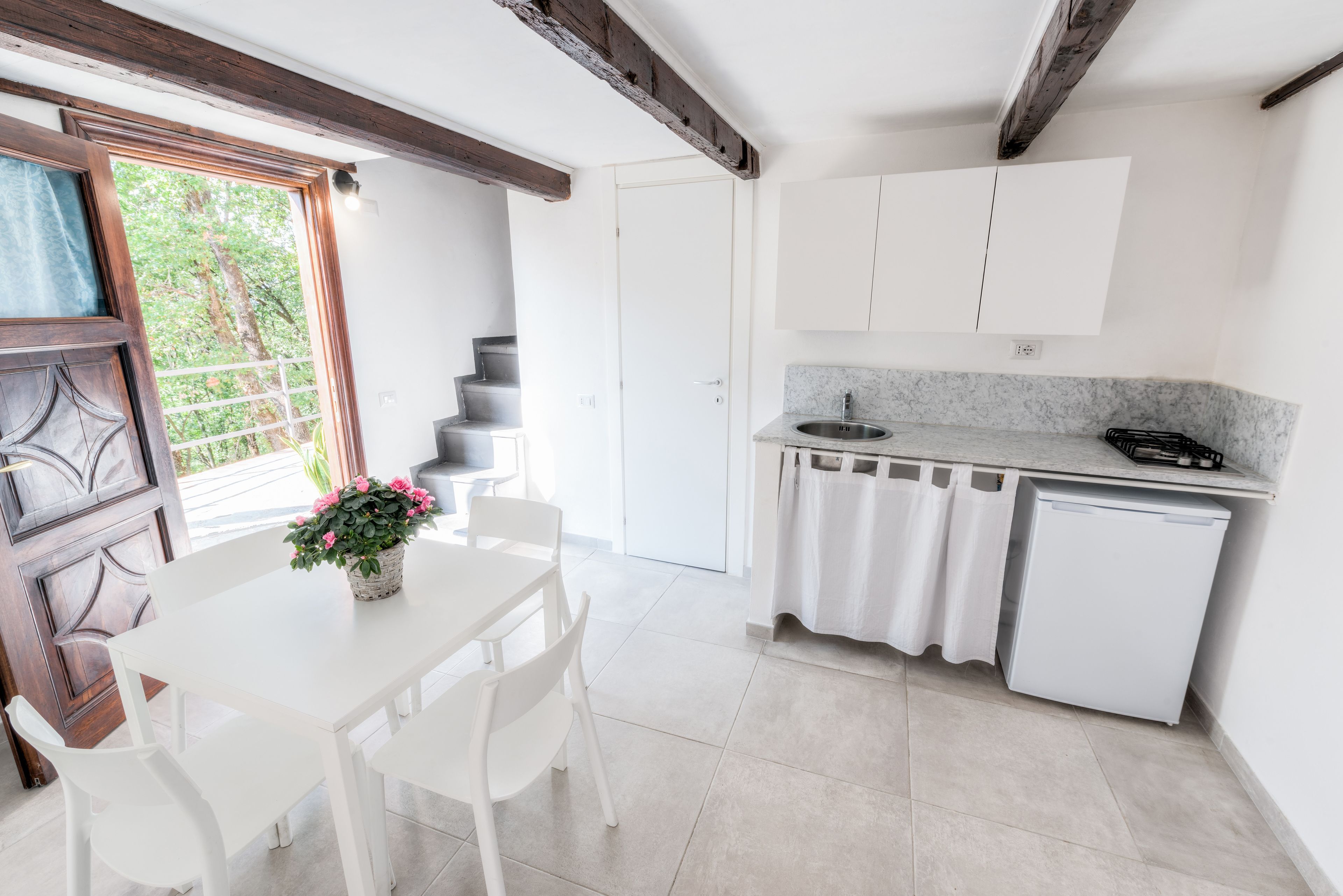 A kitchen with white cabinets, a sink, and a countertop. There is a dining table with chairs and a potted plant.