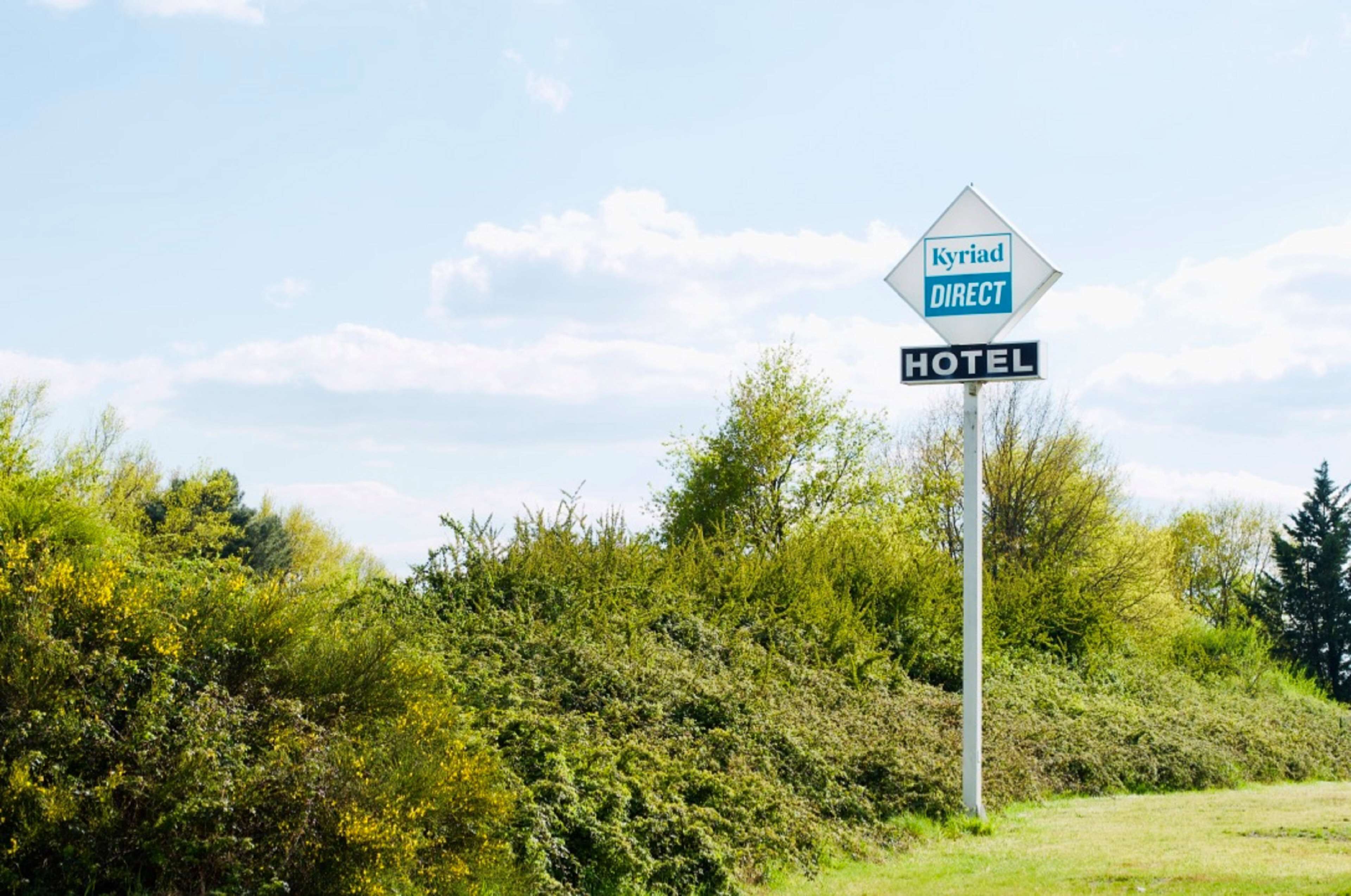 A sign for a hotel named "Kyriad Direct" with a diamond shape and a blue and white color scheme.