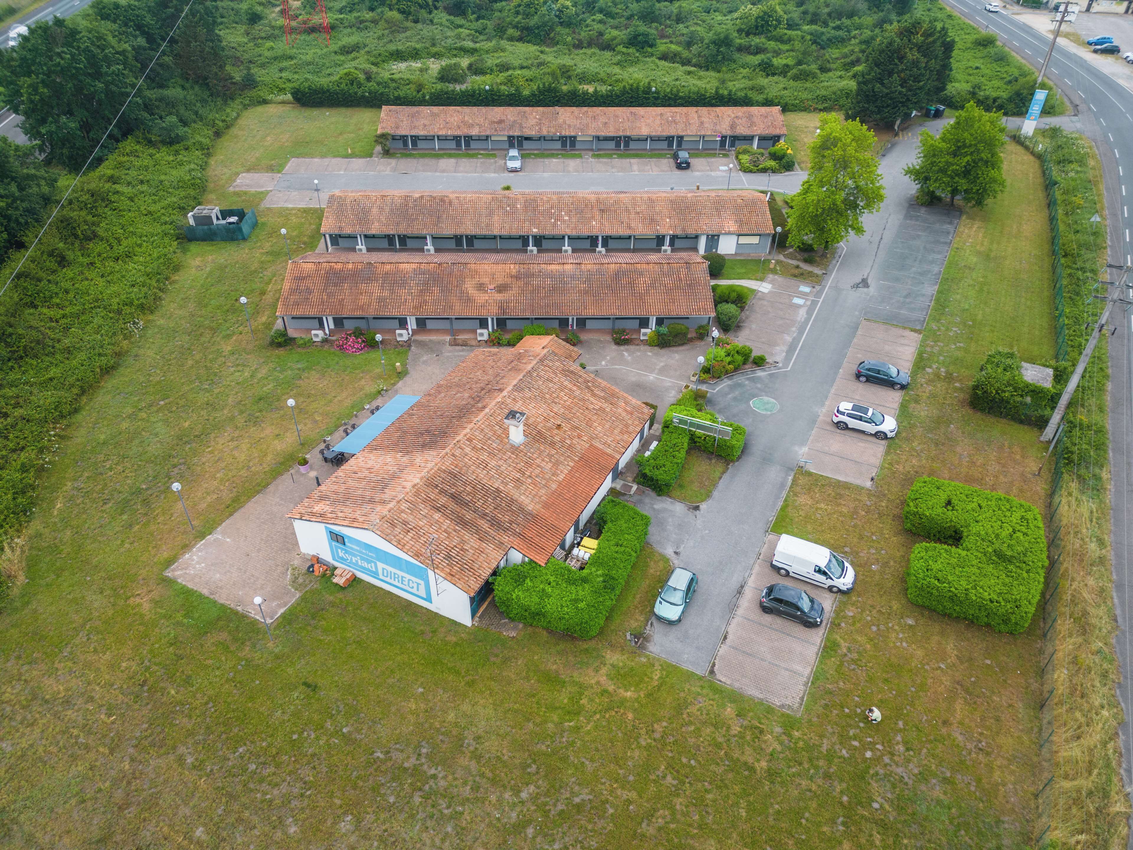 An aerial view of a hotel with two buildings, parking areas, and surrounding greenery.