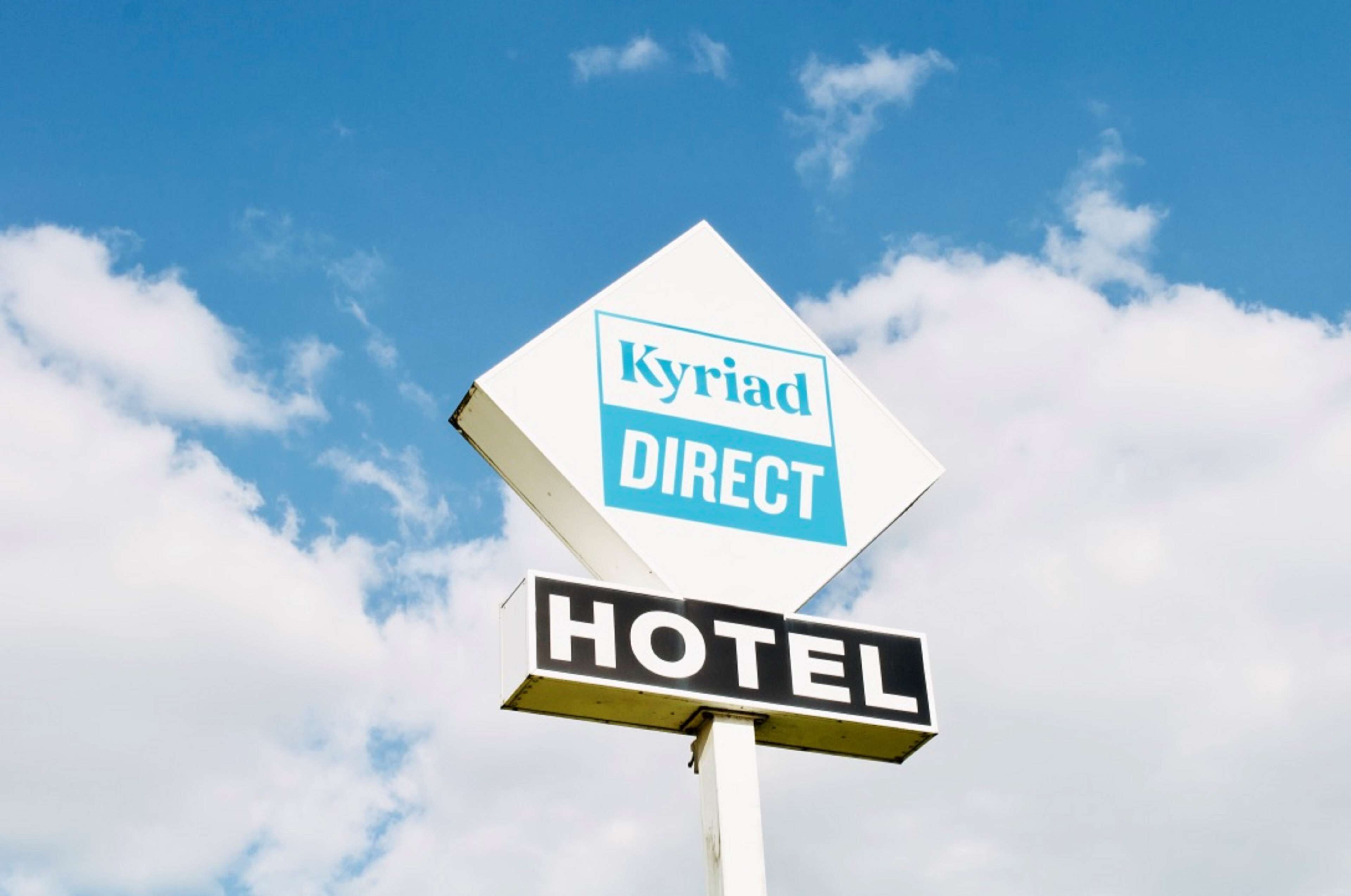 A sign for 'Kyriad Direct Hotel' with a clear sky in the background.