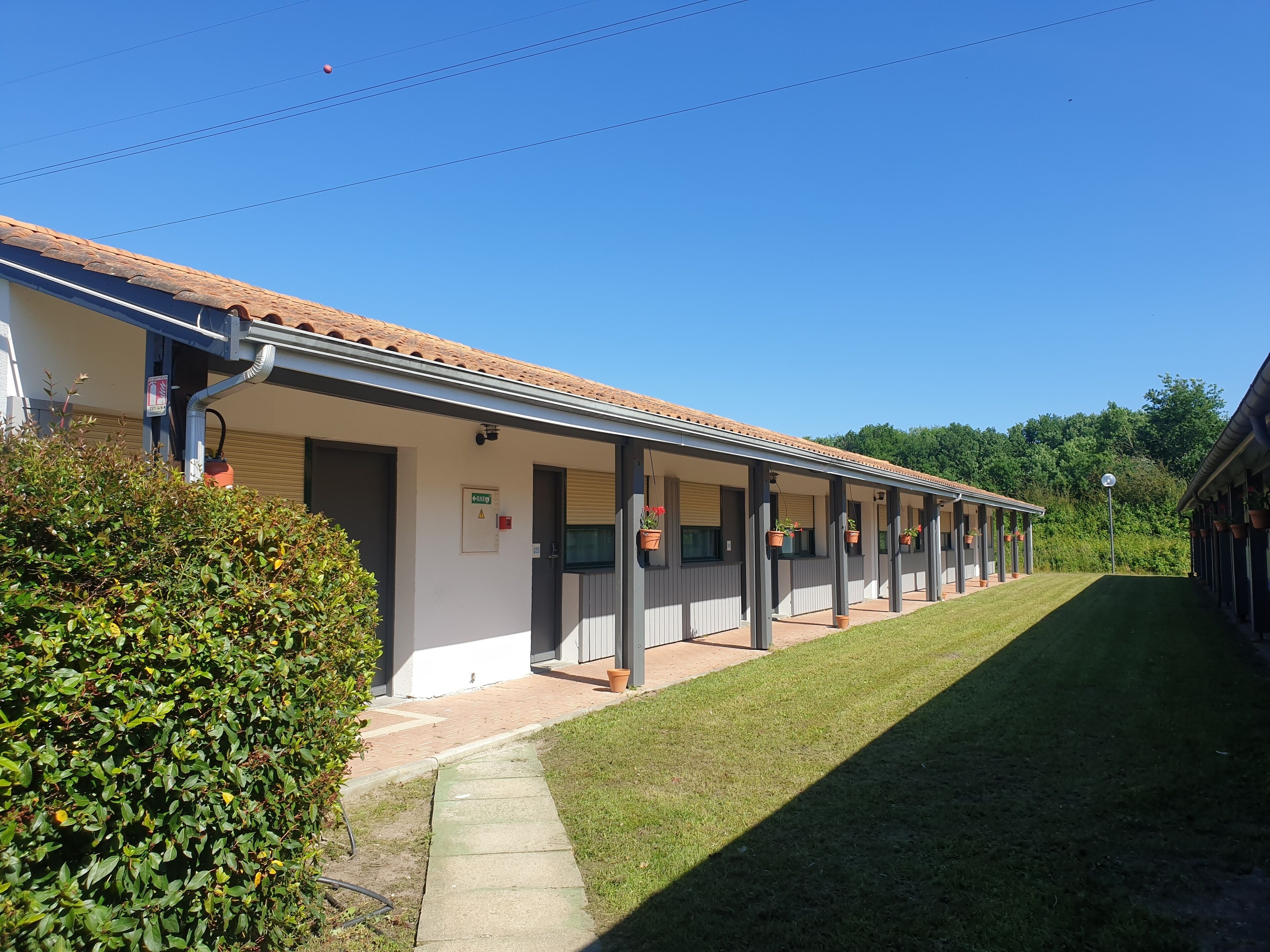Filas de habitaciones de motel de un piso con un patio cubierto, un césped y un cielo azul despejado.