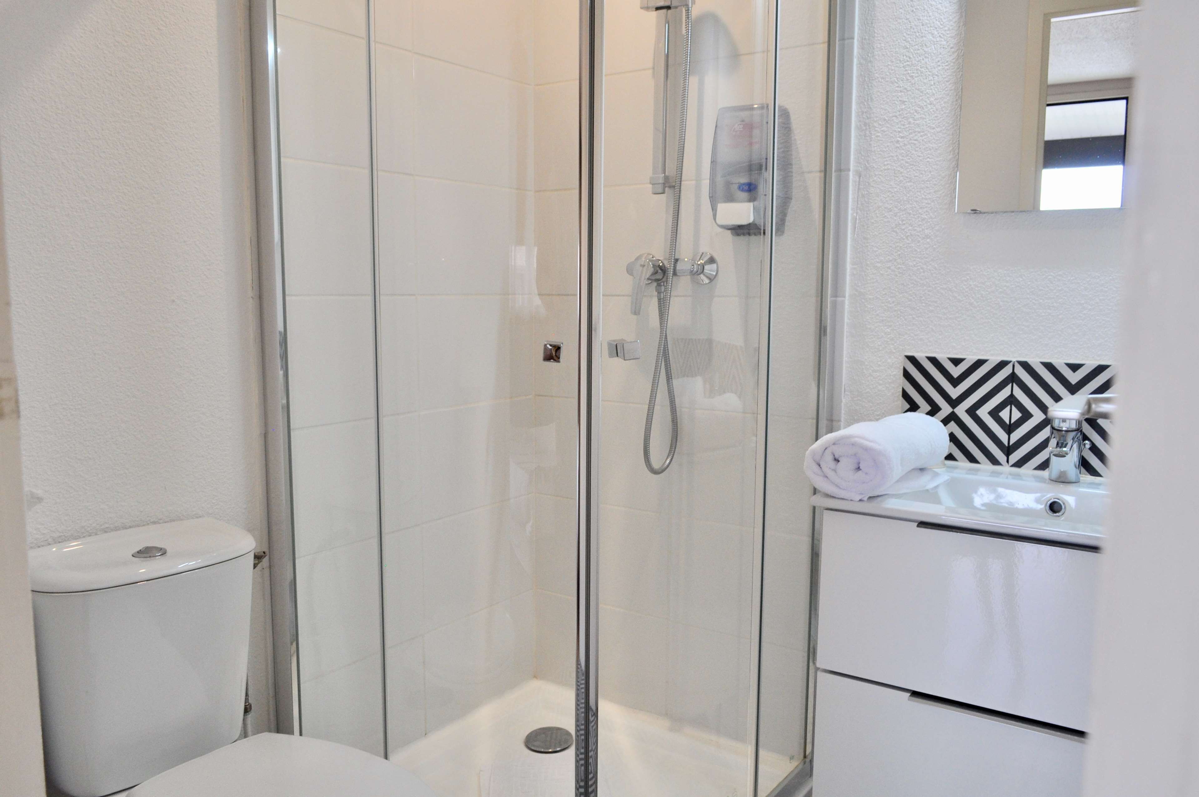 Un baño moderno con cabina de ducha de vidrio, un lavamanos blanco y un salpicadero de azulejos con estampado blanco y negro.