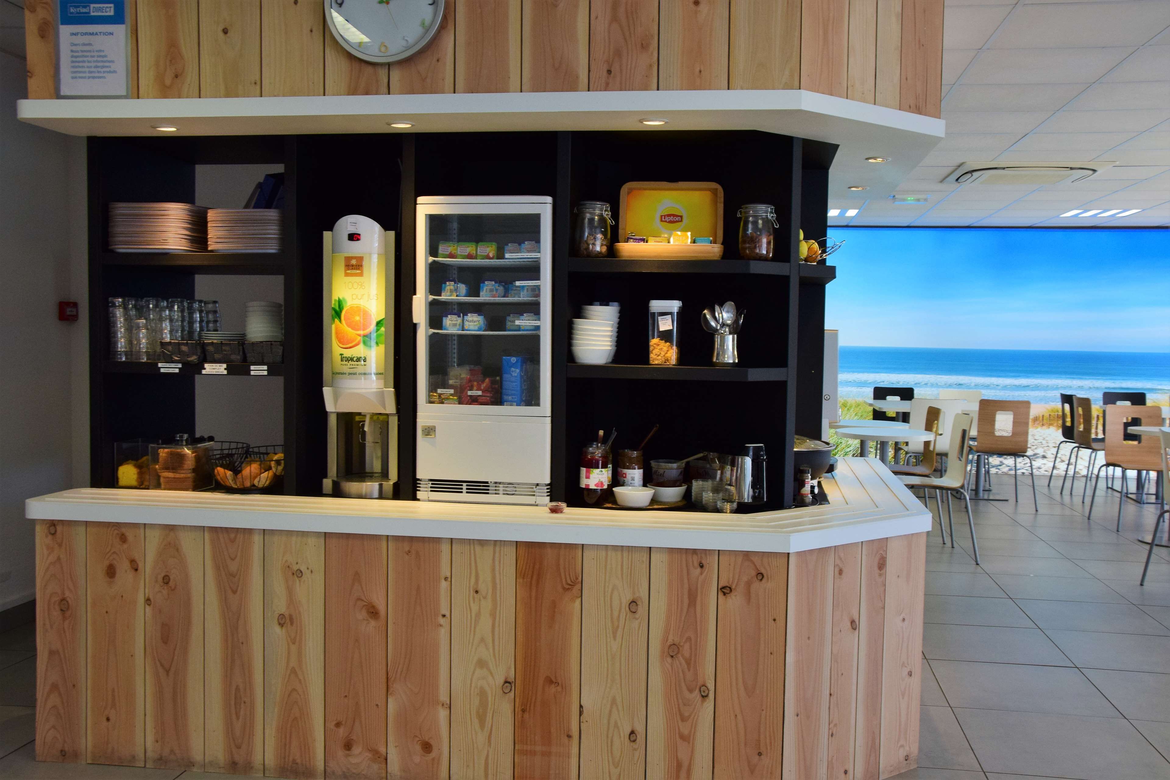 A counter with a refrigerator, shelves with glassware, and a view of the beach.