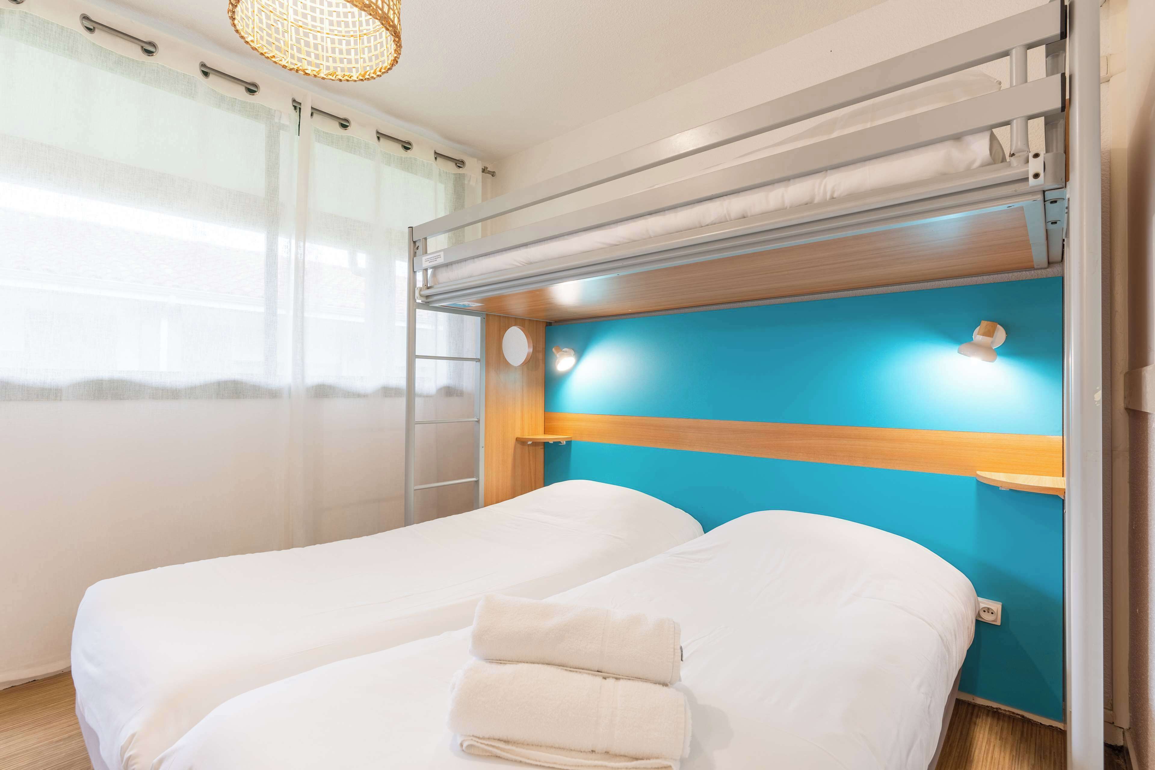 Quarto de hotel com duas camas, cabeceira de madeira e vista para o mar.