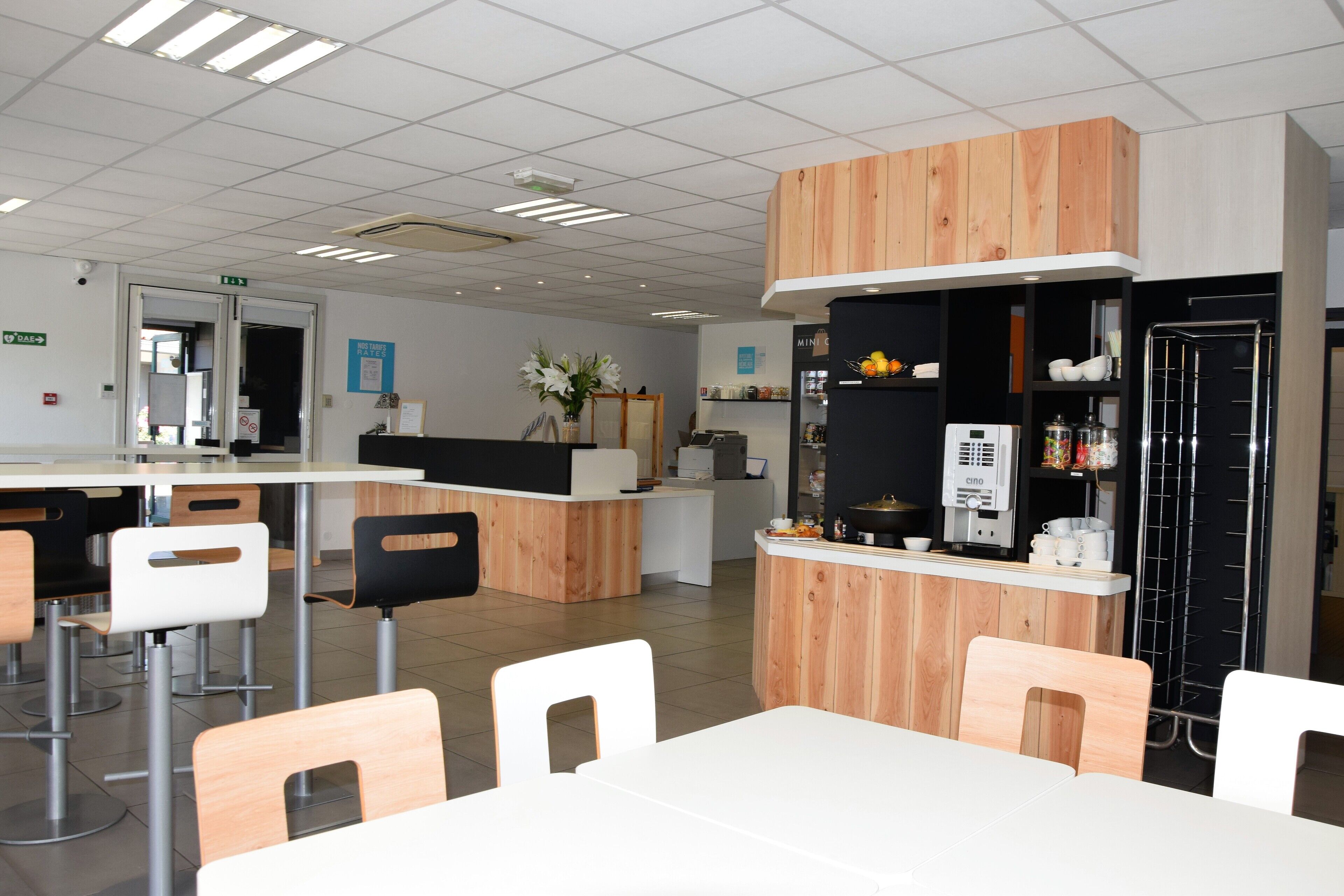 Una cafetería moderna con detalles de madera, sillas blancas y una barra con una máquina de café.