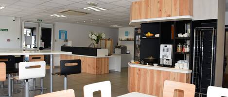 Una cafetería moderna con detalles de madera, sillas blancas y una barra con una máquina de café.
