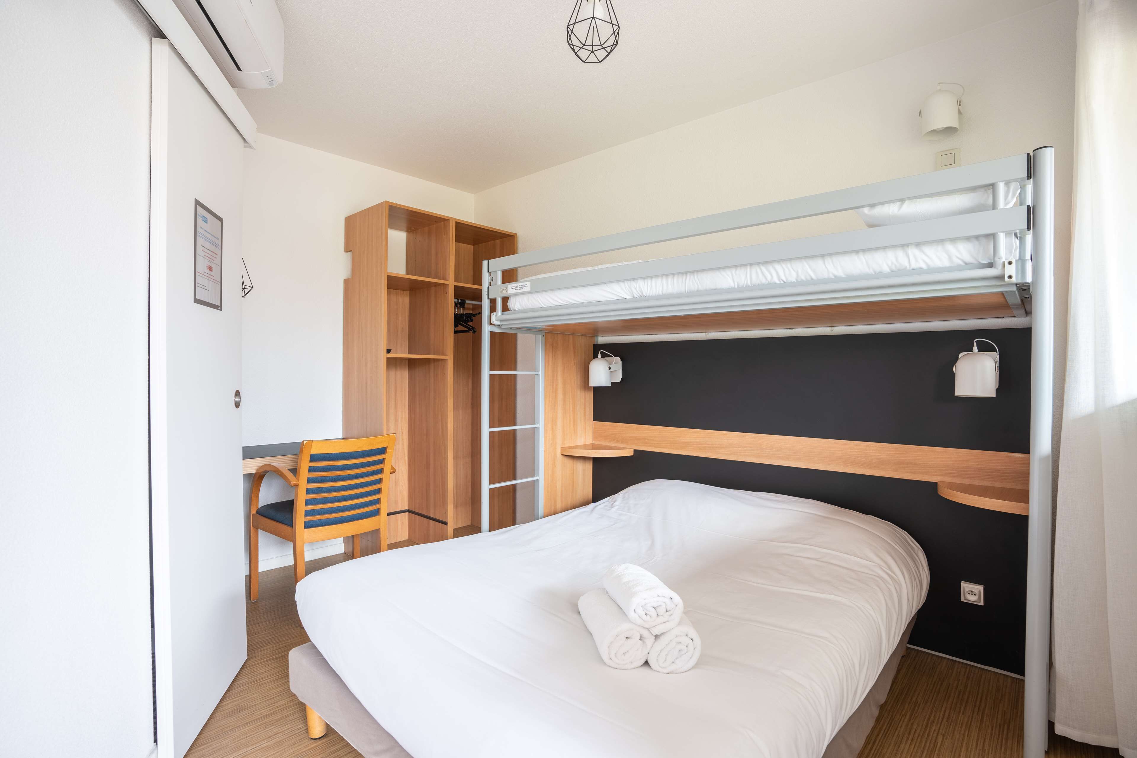 A hotel room with a bunk bed, a desk with a chair, and a wardrobe.