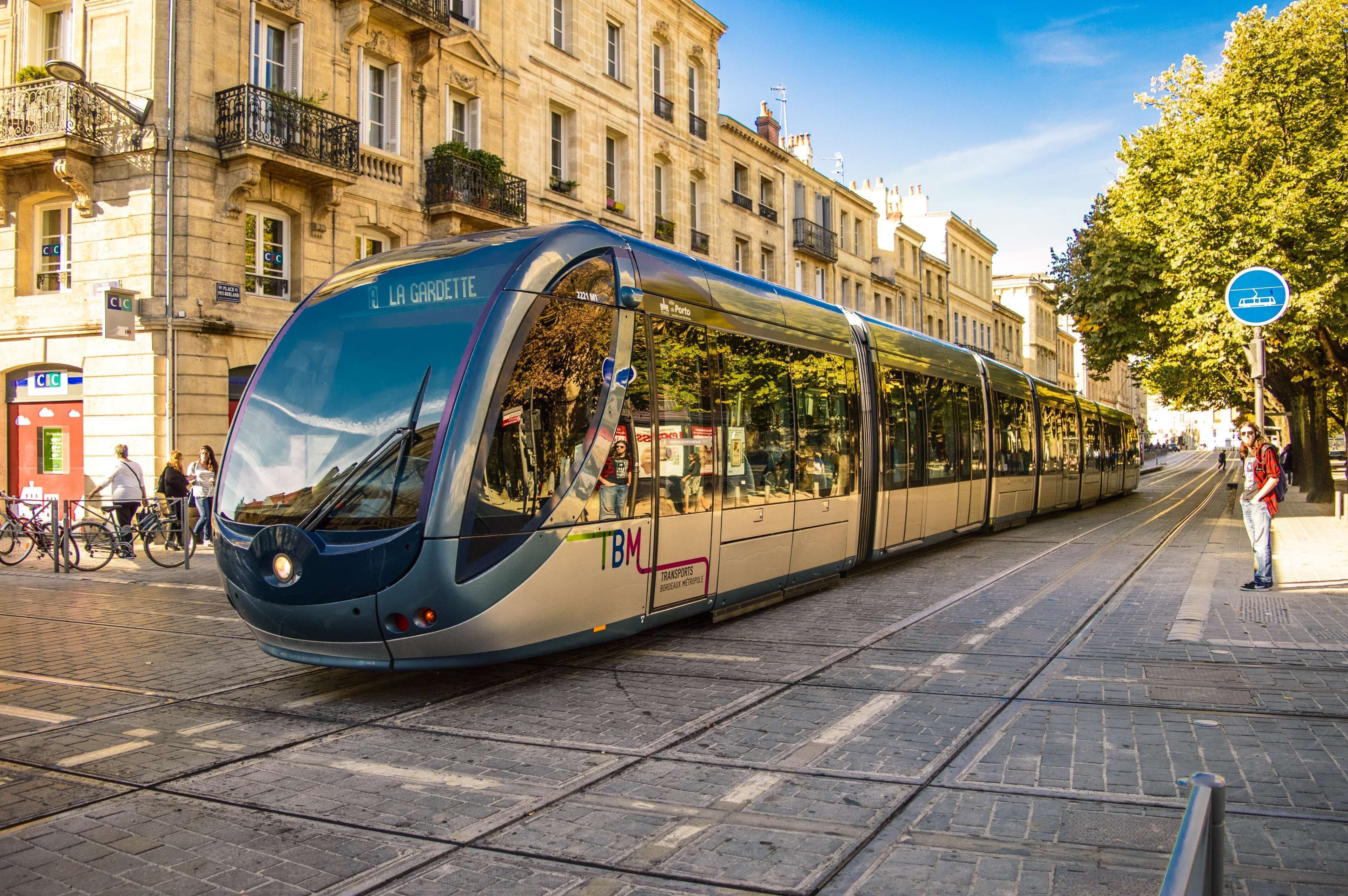 A modern tram with "La Gardette" written on the front, passing by a building with balconies and a tram stop.