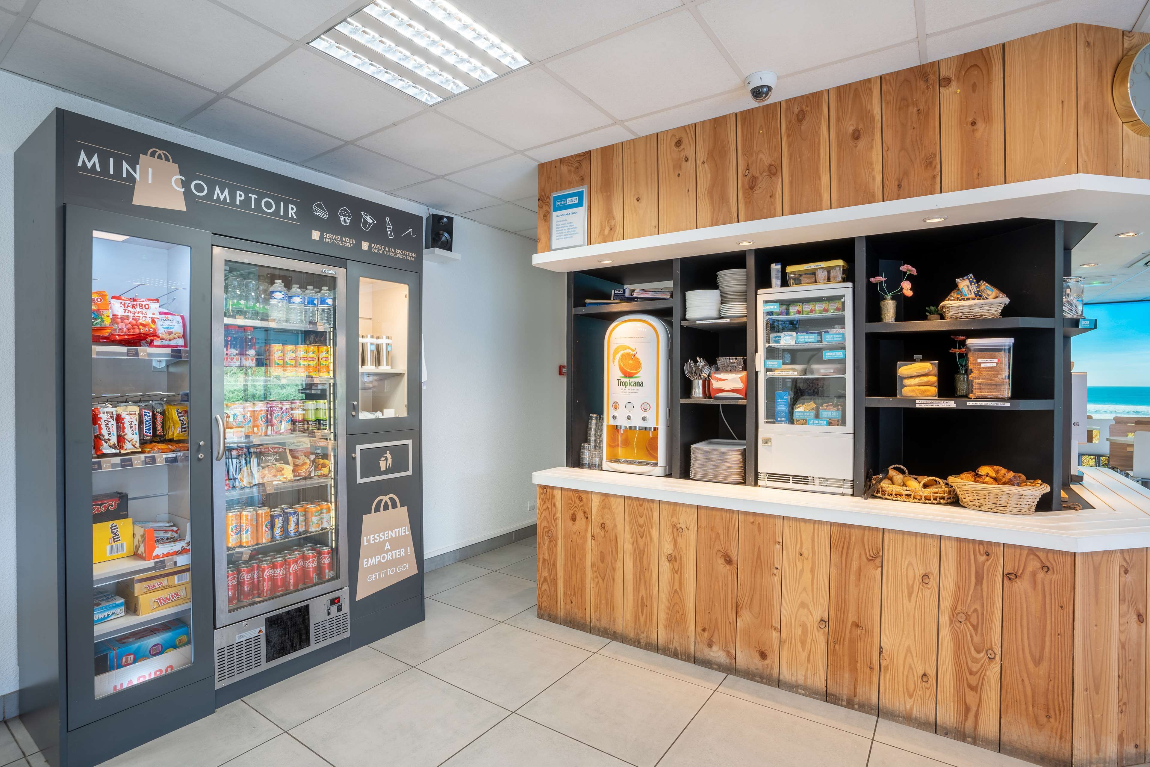 A mini convenience store with refrigerated and non-refrigerated sections, a self-service coffee machine, and a wooden counter with baskets.
