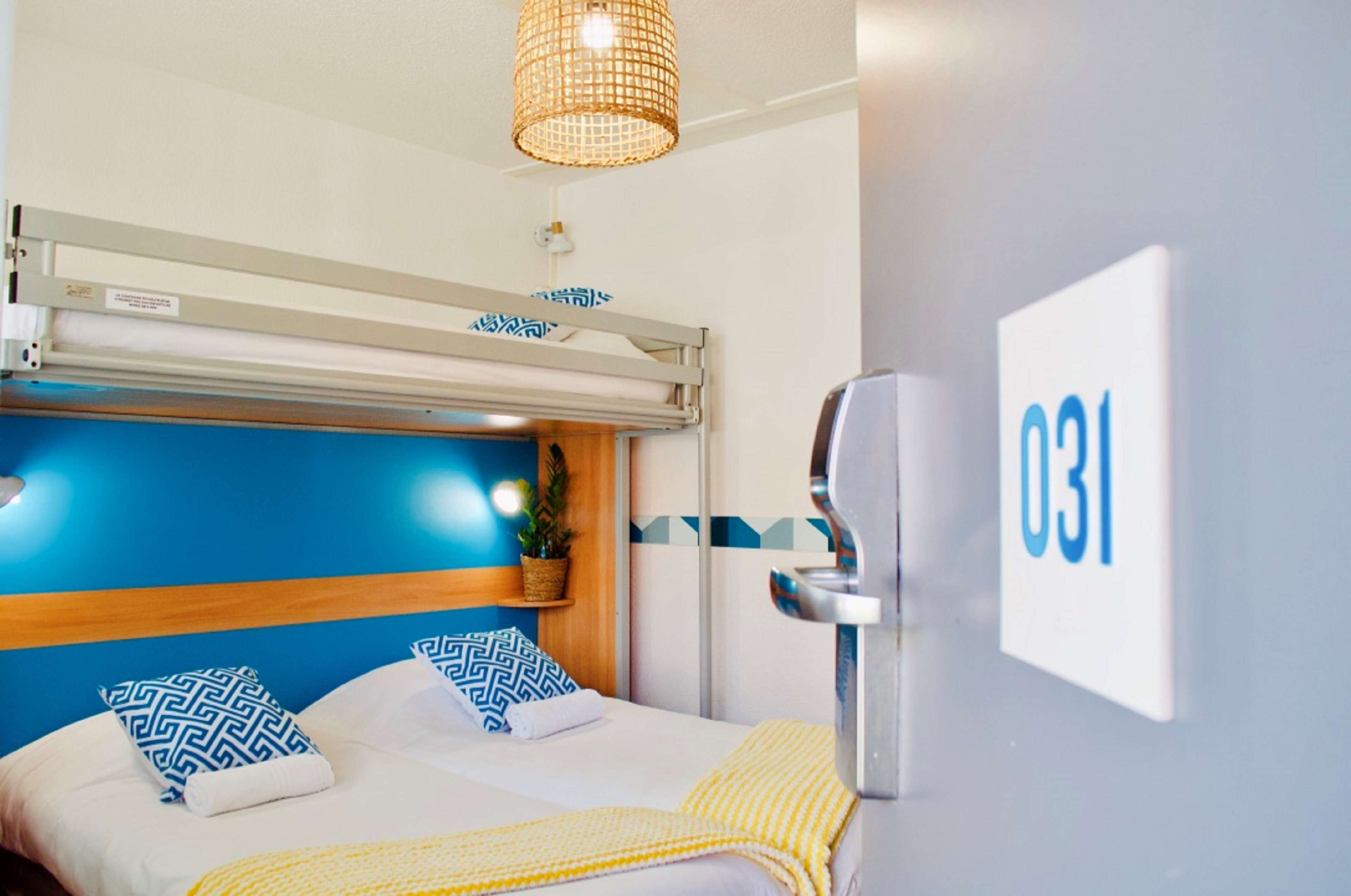 A hotel room with a bunk bed, a bedside table, a lamp, and a wall-mounted TV.