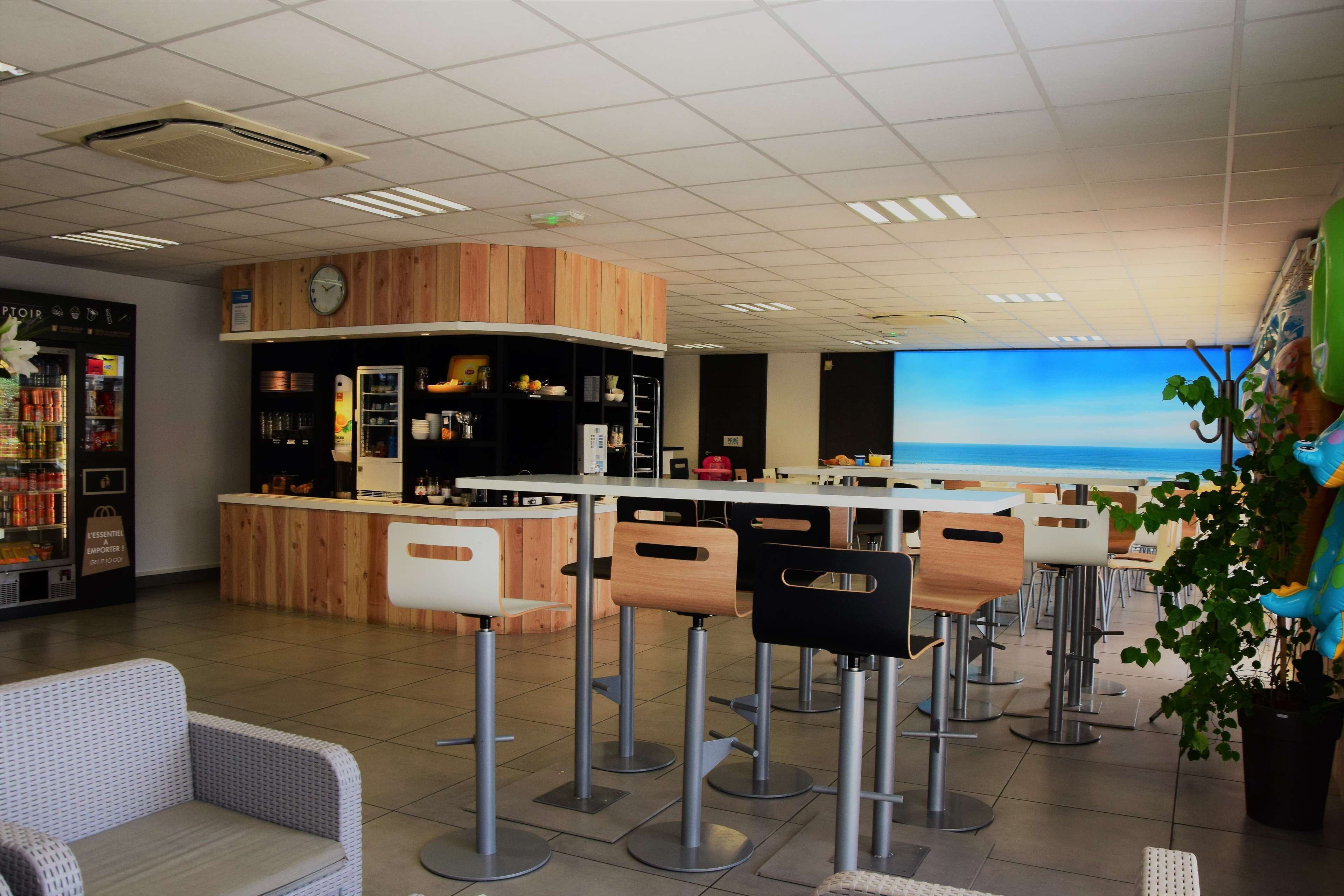 Zona de bar con mostrador de madera, taburetes y una pantalla grande que muestra una escena de playa.