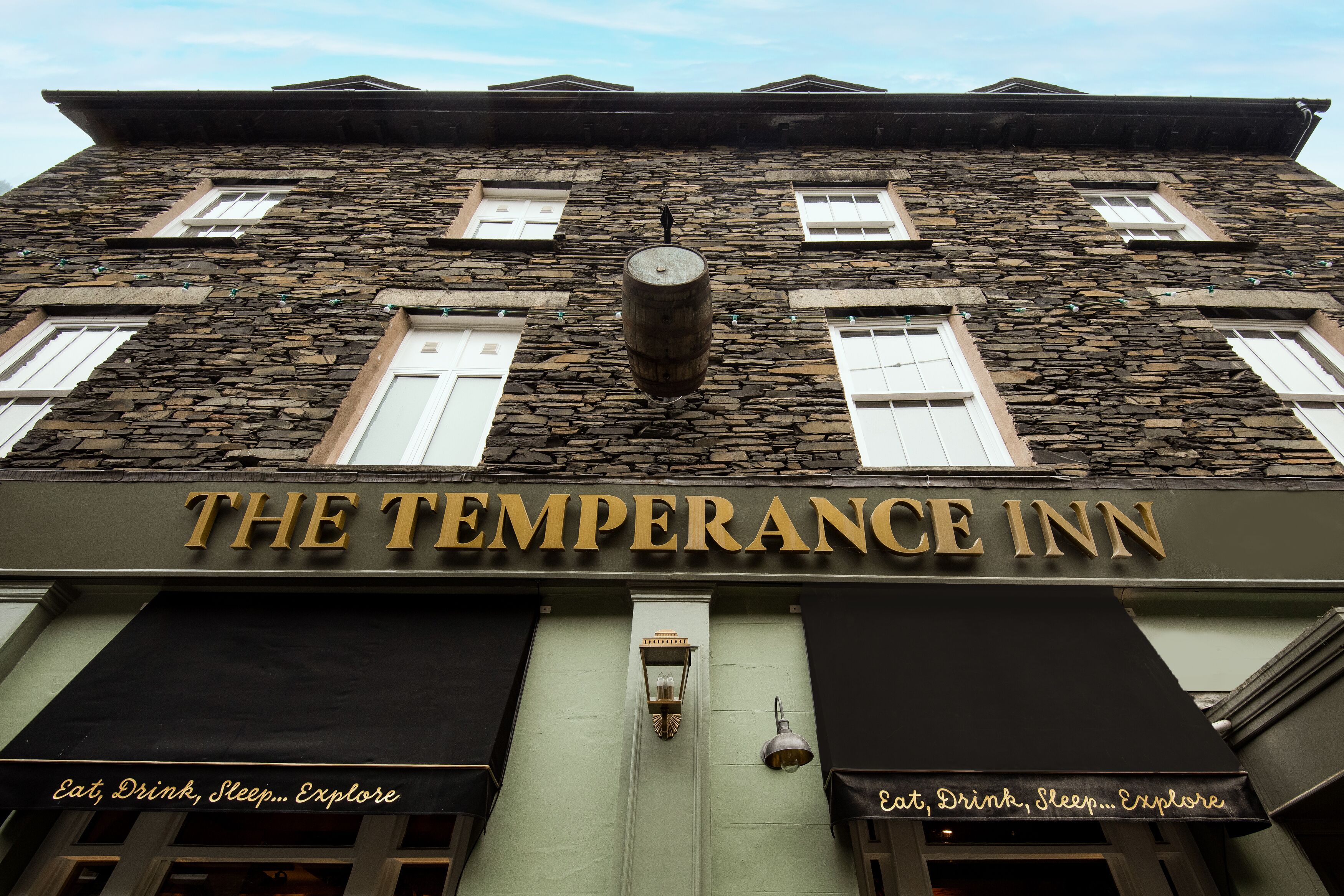 Die Fassade des The Temperance Inn aus Stein, mit zahlreichen Fenstern und einem Schild, das "The Temperance Inn Essen, Trinken, Schlafen… Entdecken" anzeigt.