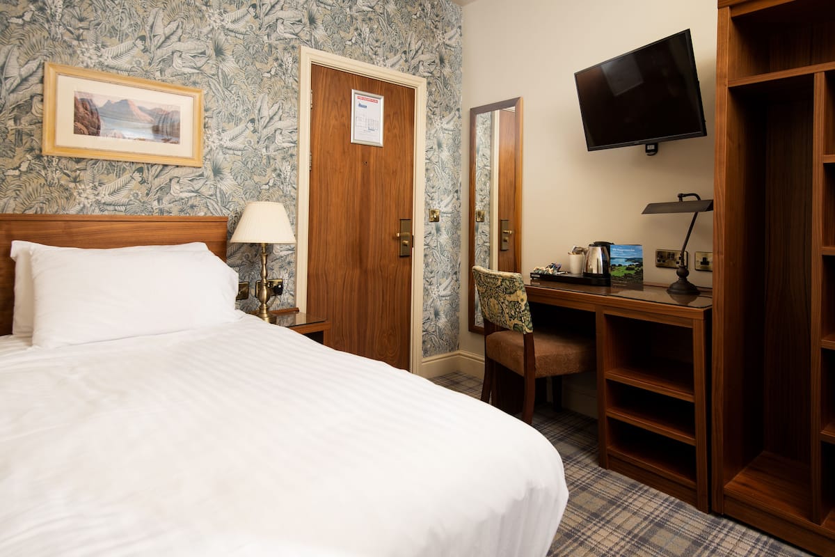 A hotel room with a bed, a desk, a chair, a television, and a wardrobe.