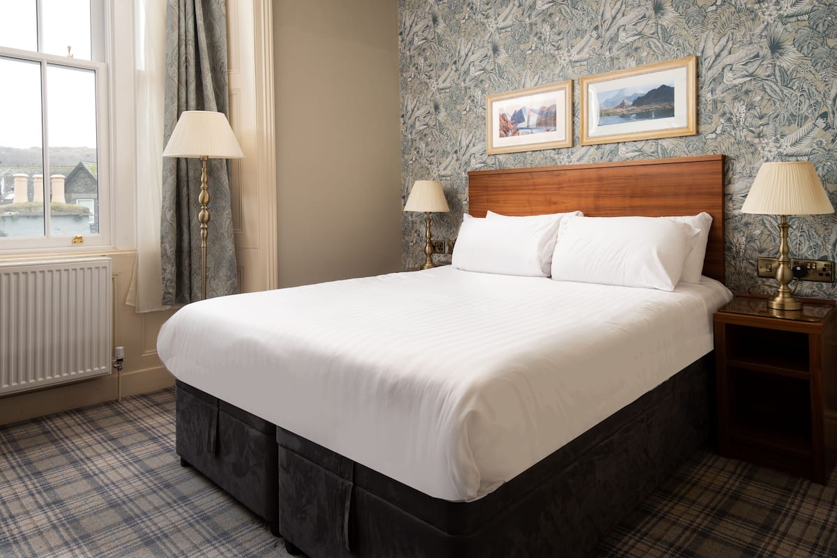A neatly made bed with white linens, a wooden headboard, and two bedside lamps.