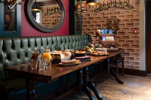 A dining area with a brick wall, a green upholstered bench, and a wooden table set with various breakfast items.