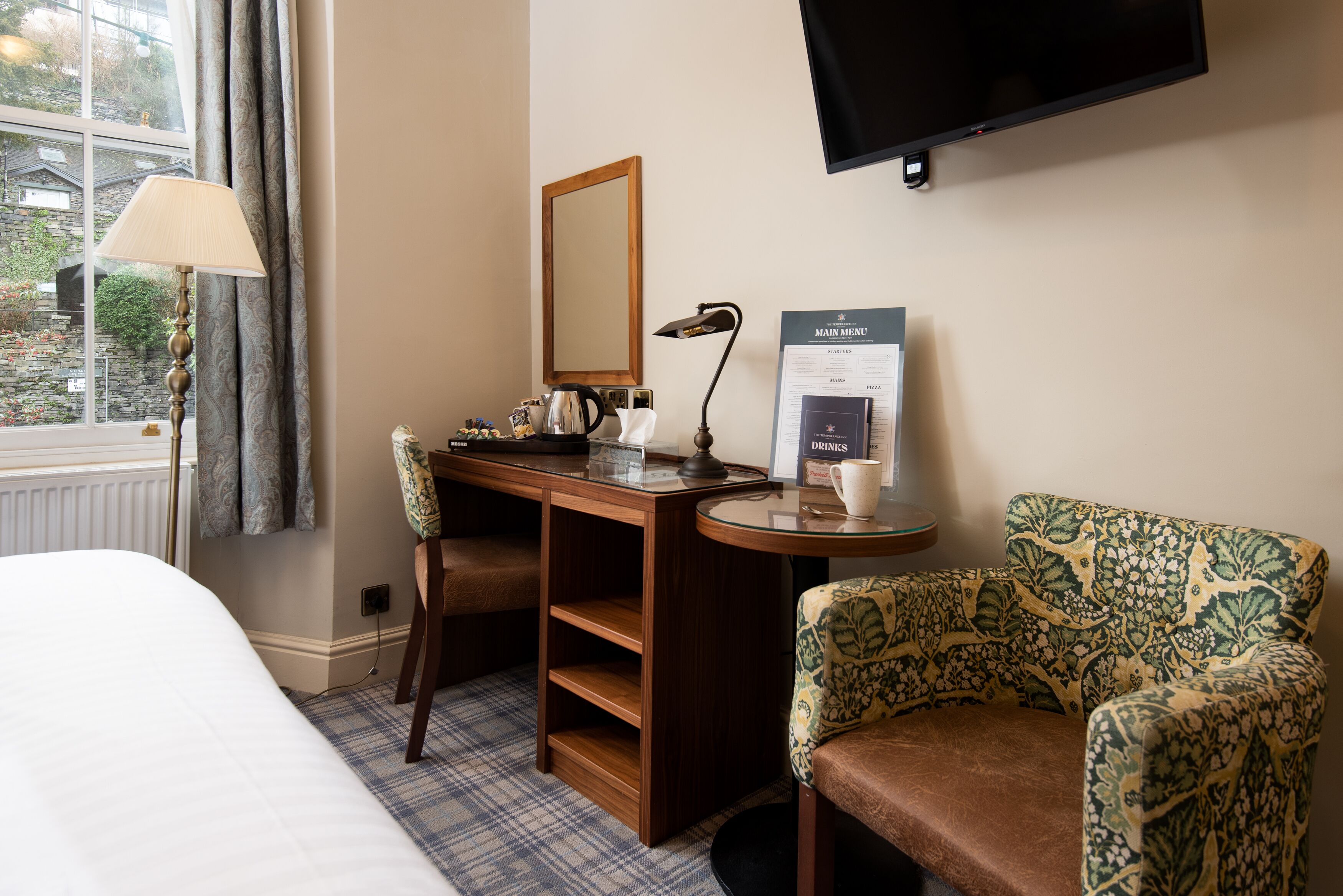 Een hotelkamer met een bed, een bureau met een lamp, een stoel, een televisie en een menubord.
