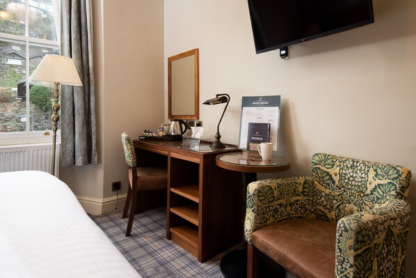 A hotel room with a bed, a desk with a lamp, a chair, a television, and a menu board.