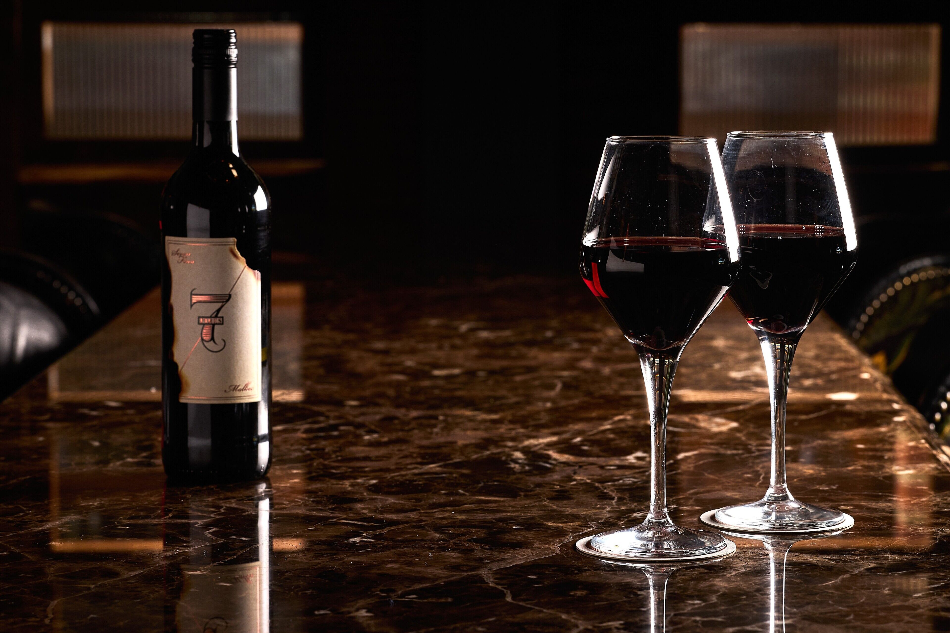A bottle of wine and two glasses on a marble surface.