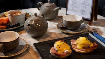 A breakfast setting with a teapot, cups, and a plate with eggs benedict.