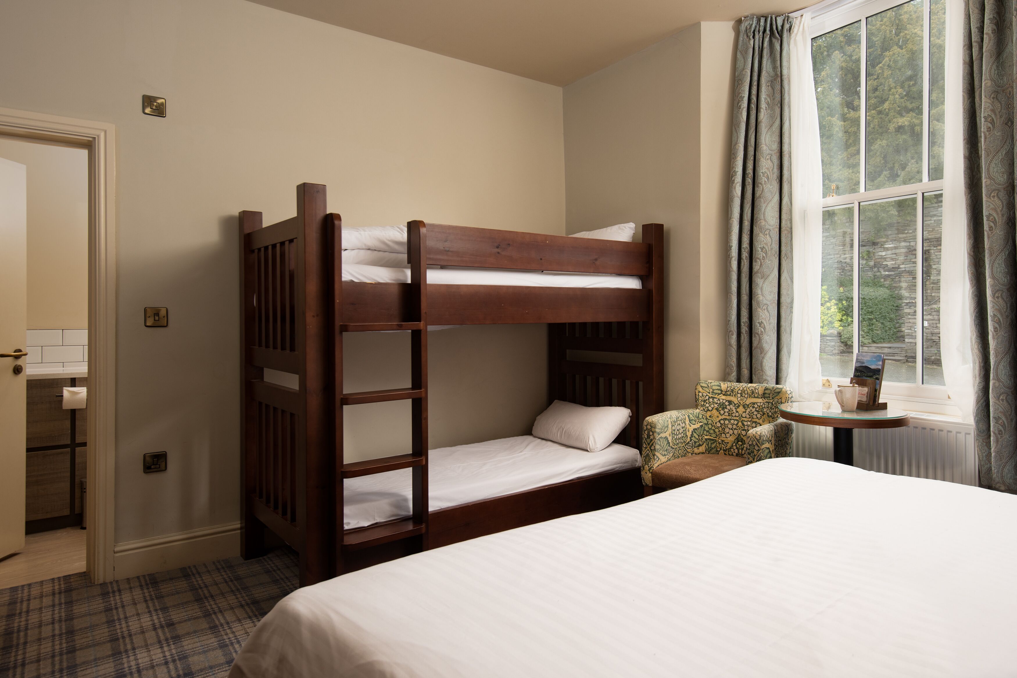 Een kamer met een stapelbed, een enkel bed, een stoel en een kleine tafel bij een raam.