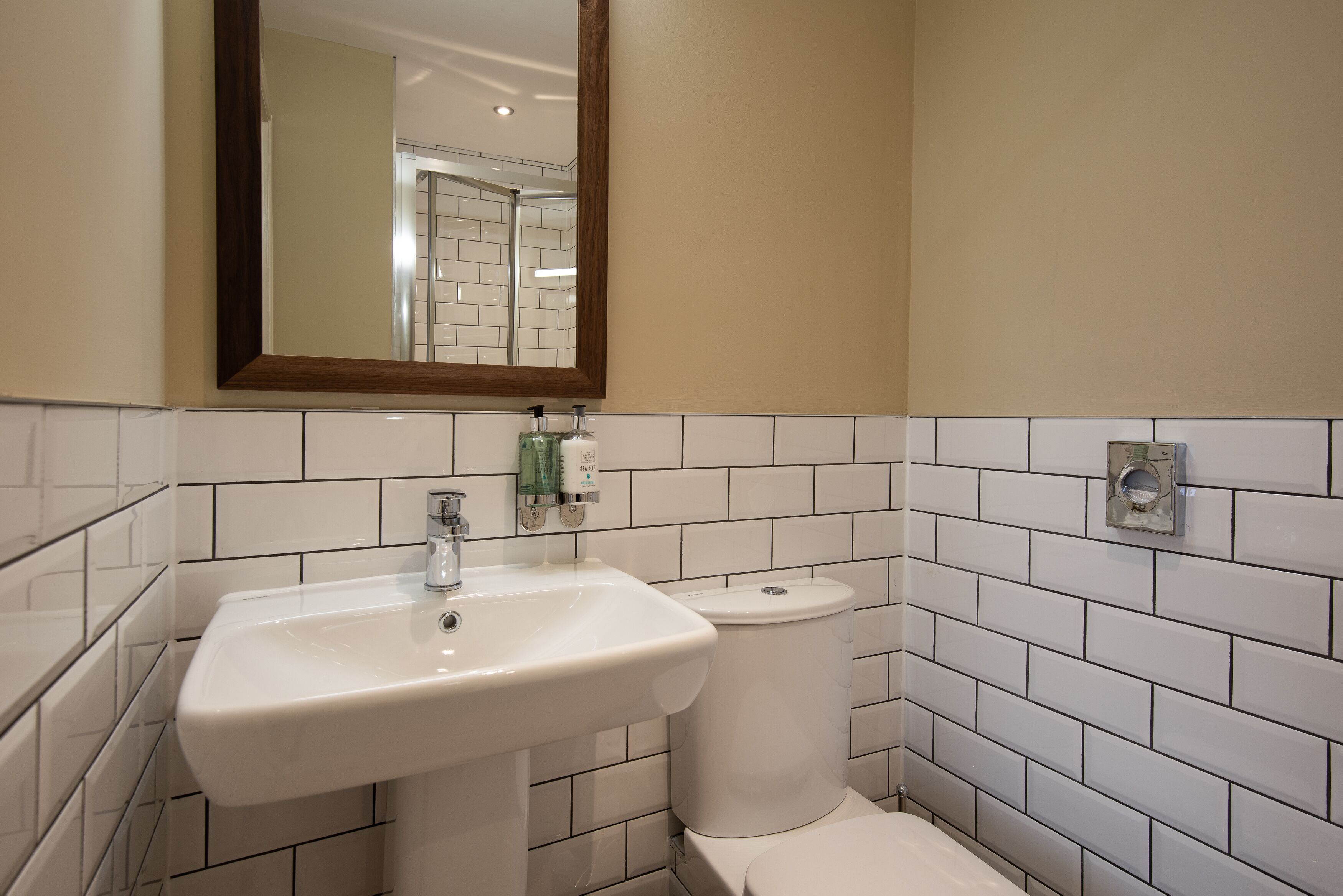 Un baño con lavamanos blanco, inodoro y paredes con azulejos.