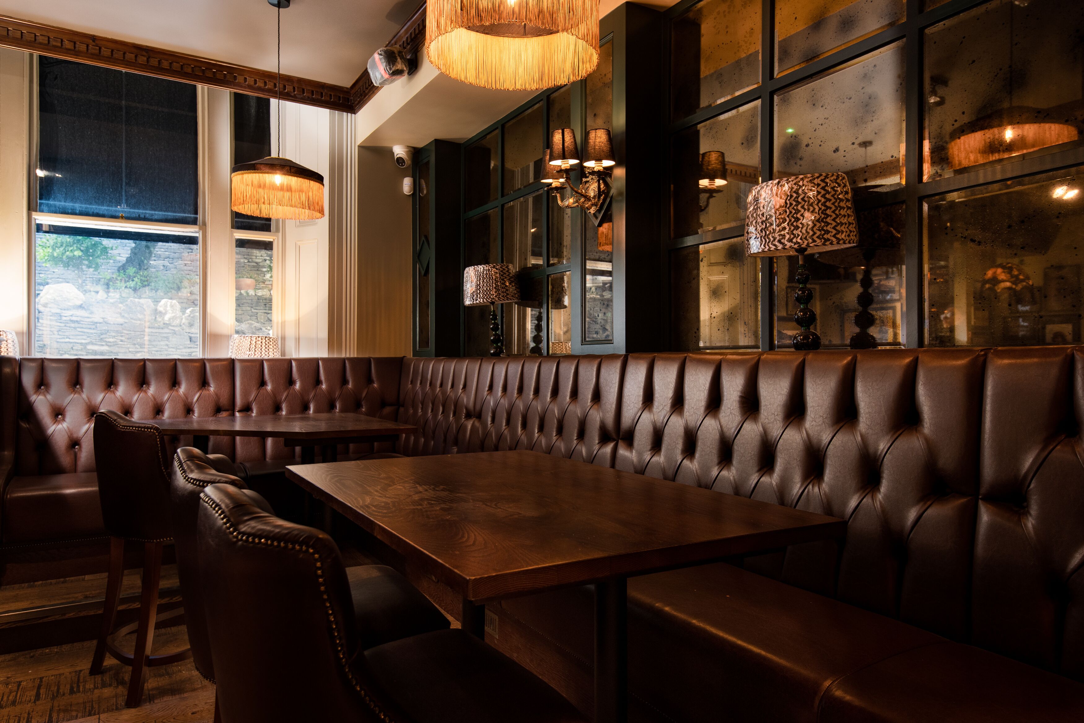 A restaurant with leather booths, wooden tables, and pendant lighting.