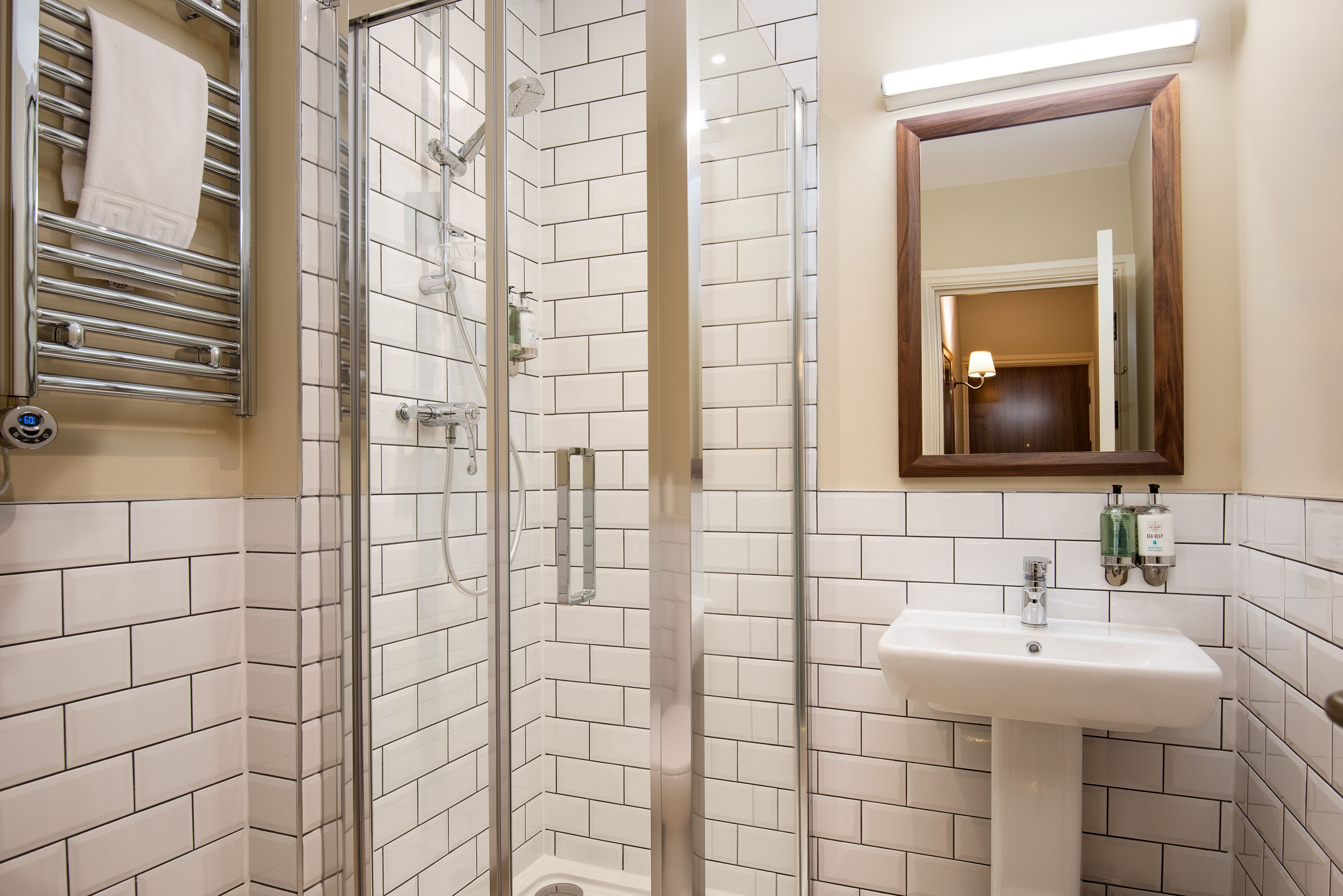 Un bagno con cabina doccia in vetro, un lavandino bianco e uno specchio con cornice in legno.