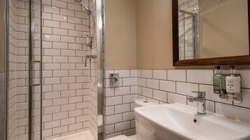 A bathroom with a glass-enclosed shower, white tiled walls, a white sink, and a mirror with a wooden frame.