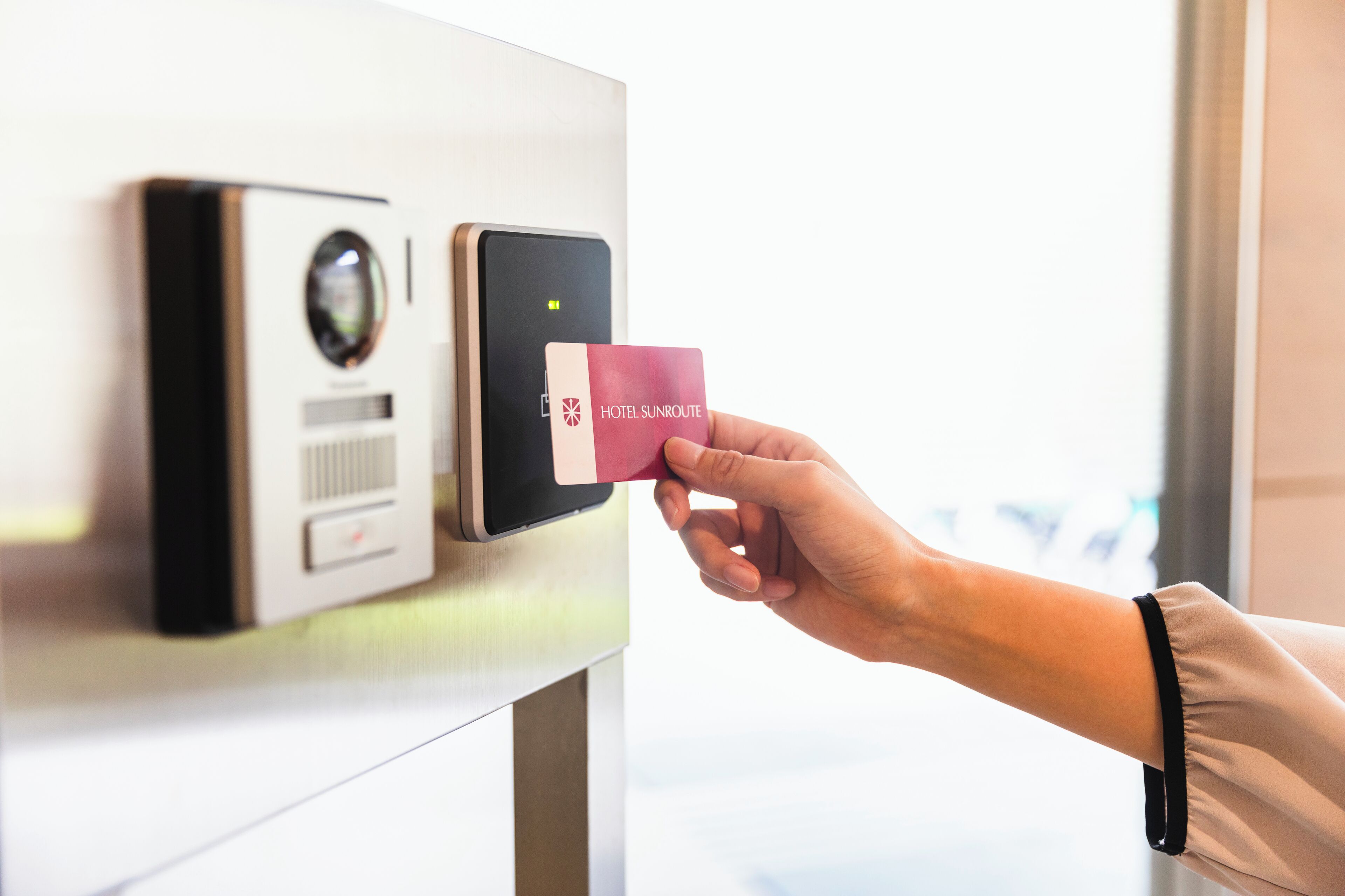 A hand holding a Hotel SunRoute card near a card reader, indicating a check-in or payment process.