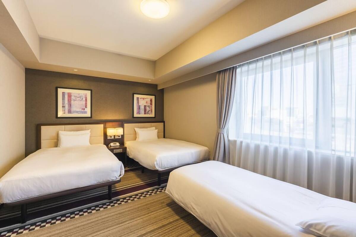 Une chambre d’hôtel avec deux lits, un tapis à carreaux, une table de chevet avec une lampe et deux tableaux encadrés au mur.