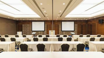 A conference room with multiple tables and chairs, a large screen, and a podium.