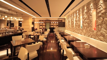 A modern restaurant with a long counter, multiple tables, and a stone accent wall.