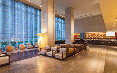 A spacious lobby with a reception desk, comfortable seating area, and large windows offering views of the city.