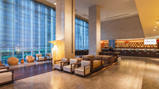 Eine geräumige Lobby mit einer Rezeption, einer gemütlichen Sitzecke und großen Fenstern mit Blick auf die Stadt.