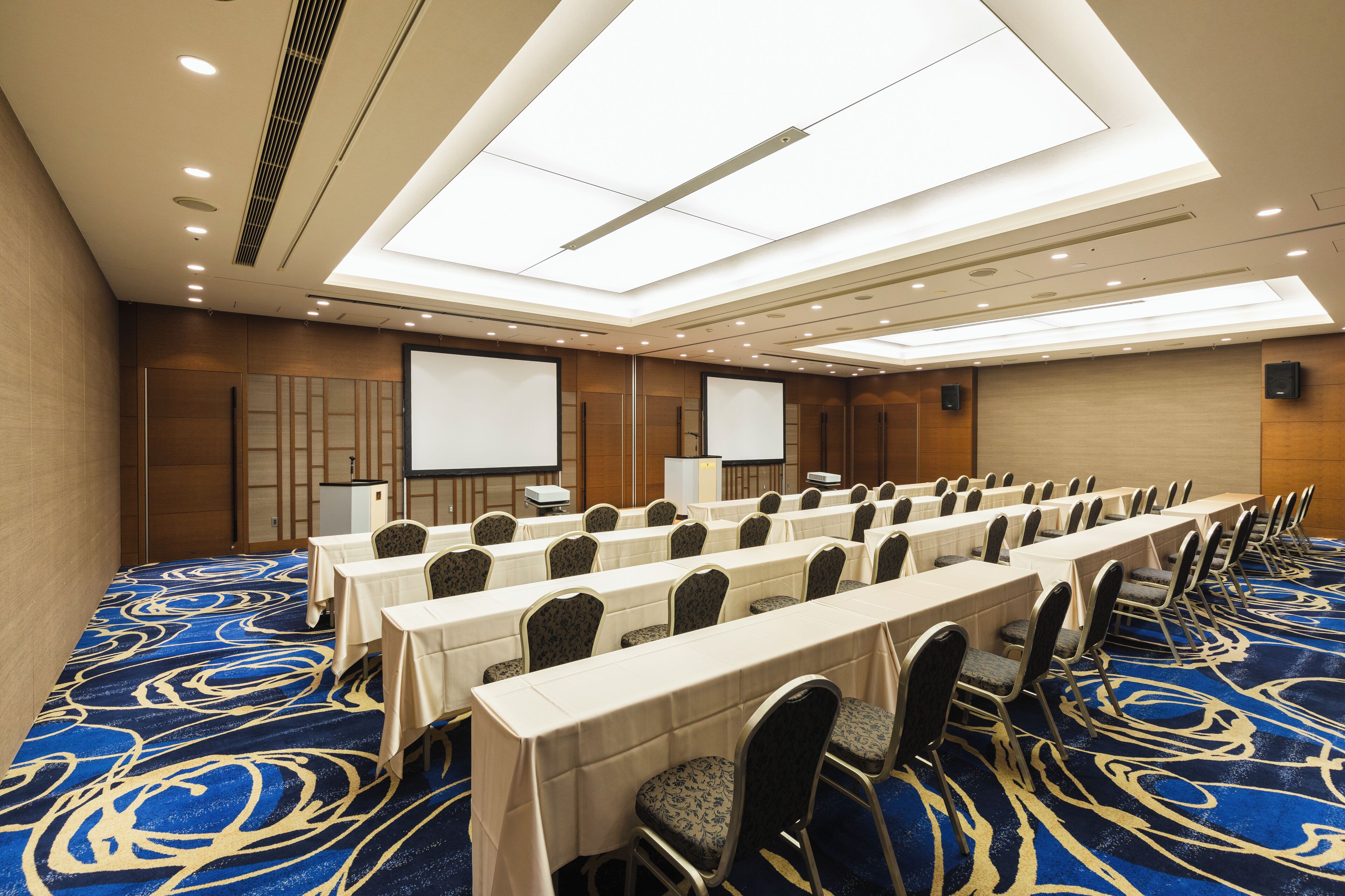 A conference room with long tables and chairs, a projector screen, and a presentation screen.