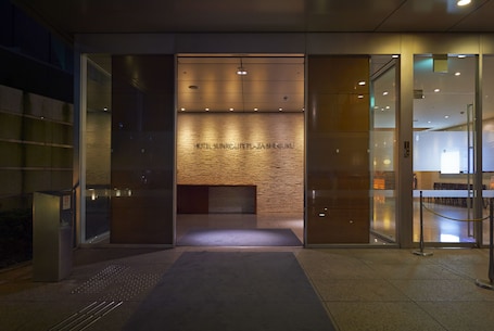 A modern hotel entrance with a wooden wall and glass doors, a reception desk, and a visible name sign.
