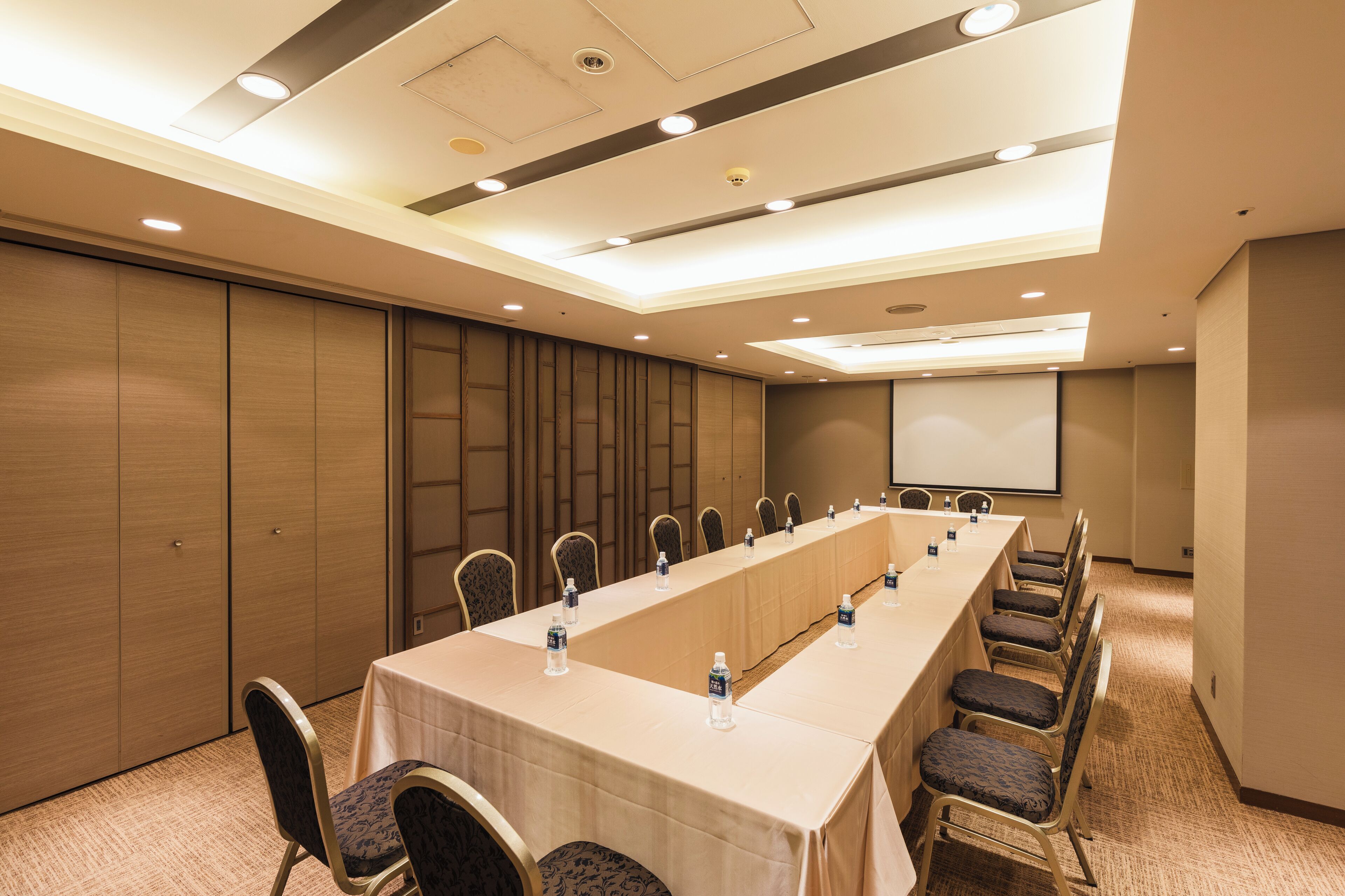 A conference room with a long table, chairs, and a projector screen.
