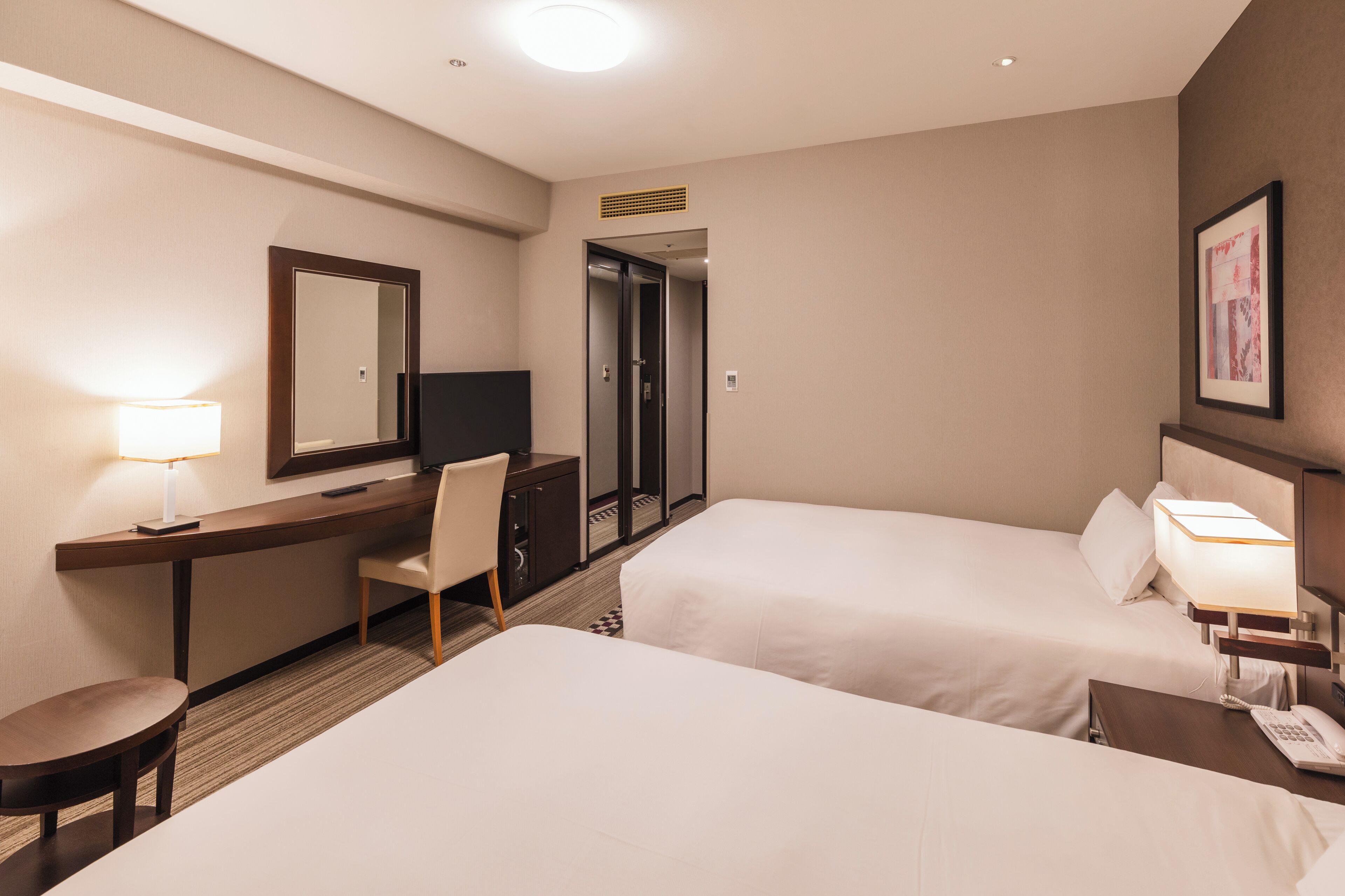A hotel room with two beds, a desk with a chair, a TV, and a lamp.