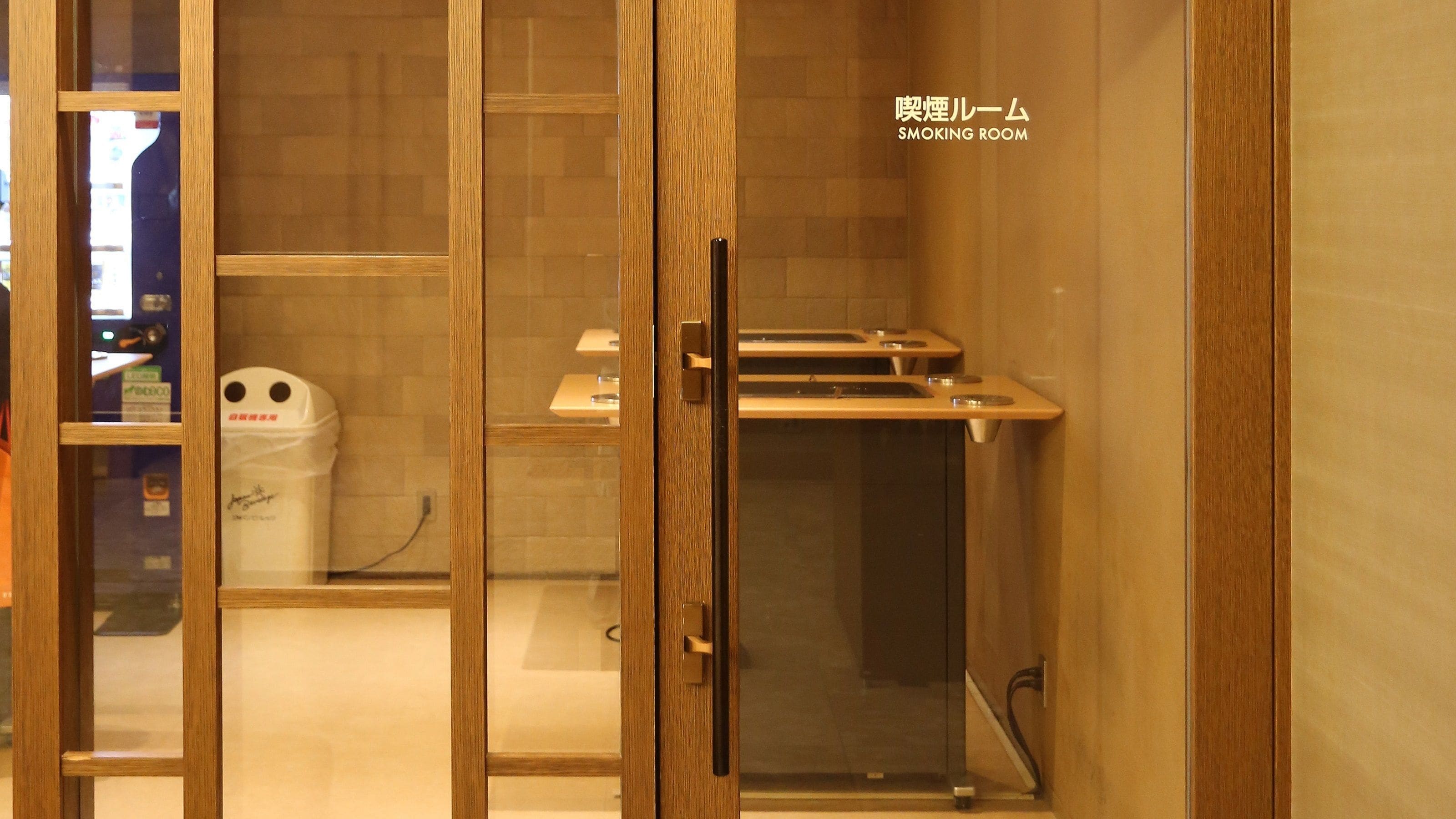 Una sala para fumadores con puerta de madera, un lavamanos pequeño y un cubo de basura.
