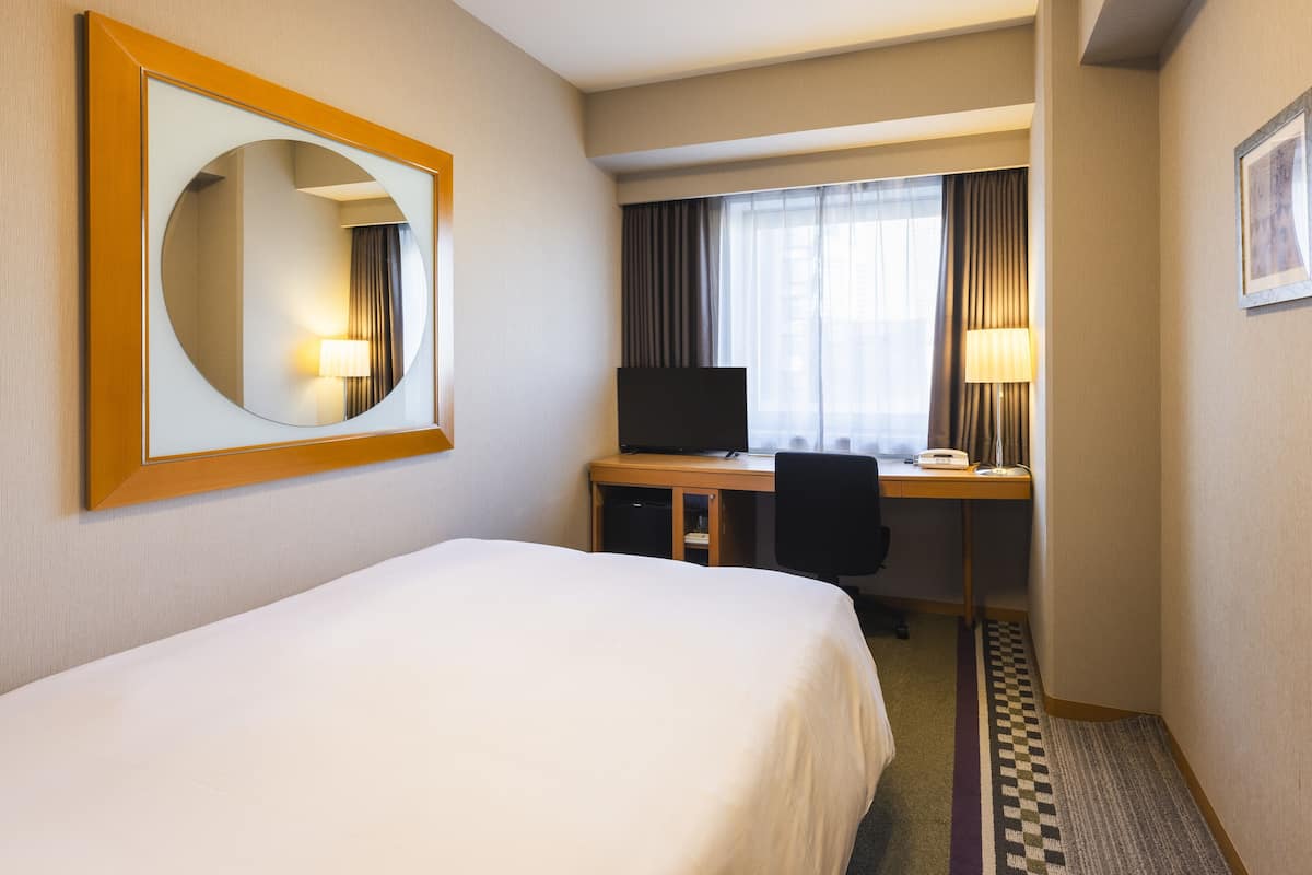 Une chambre d’hôtel équipée d’un lit, d’un bureau, d’une chaise, d’une télévision et d’un grand miroir.